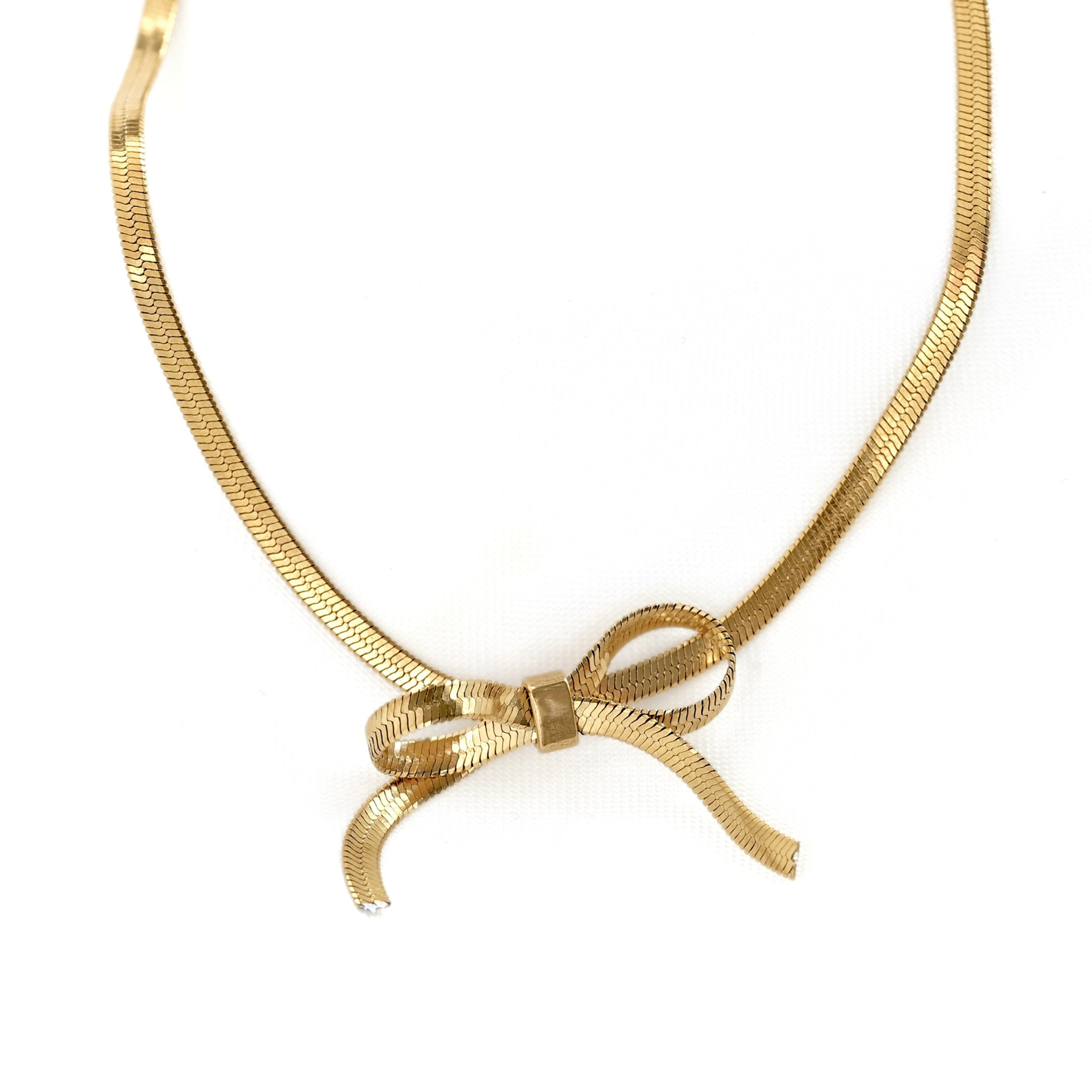 A thin gold herringbone chain necklace featuring a central bow charm, displayed on a clean white background.