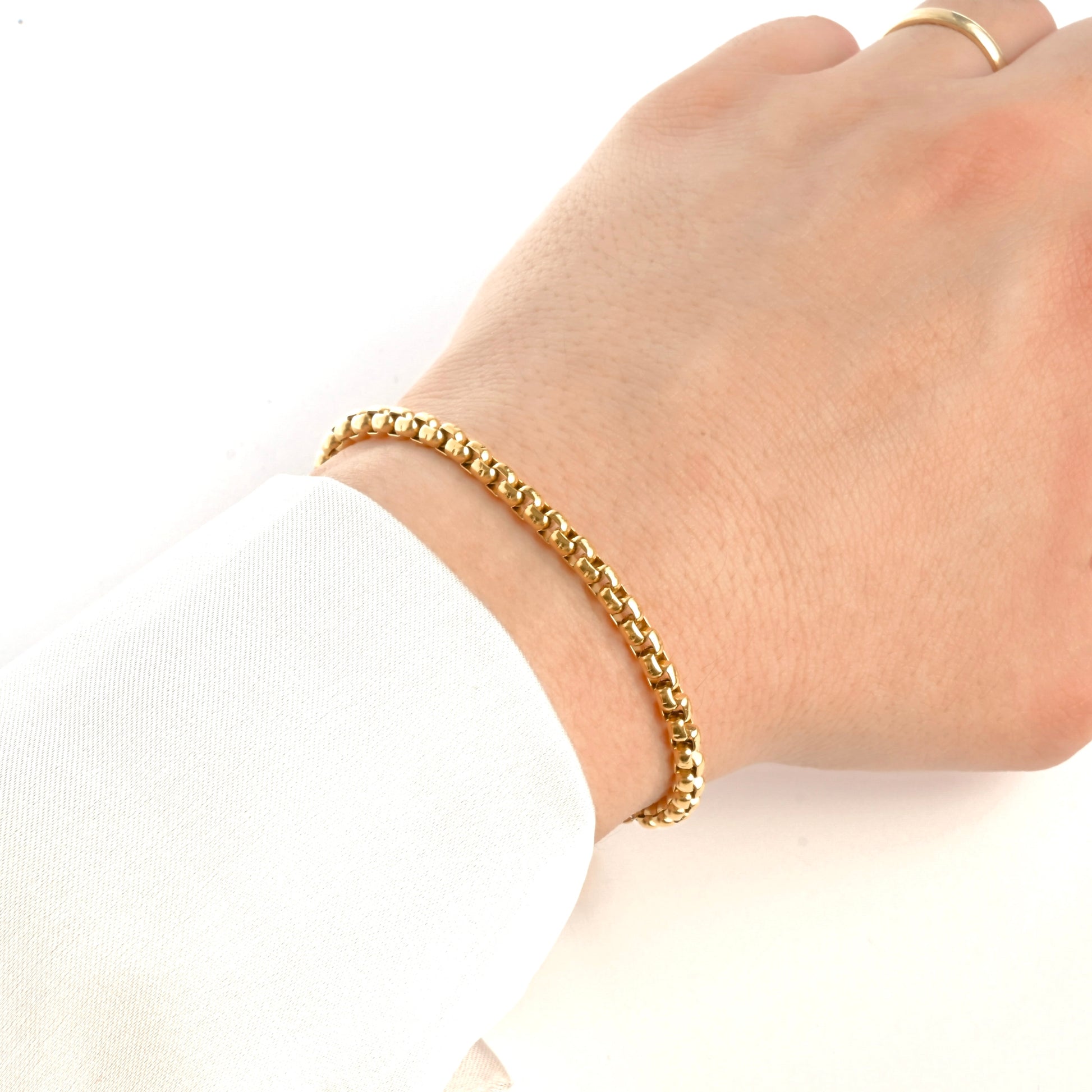 Gold rounded box chain bracelet on a wrist with a plain background