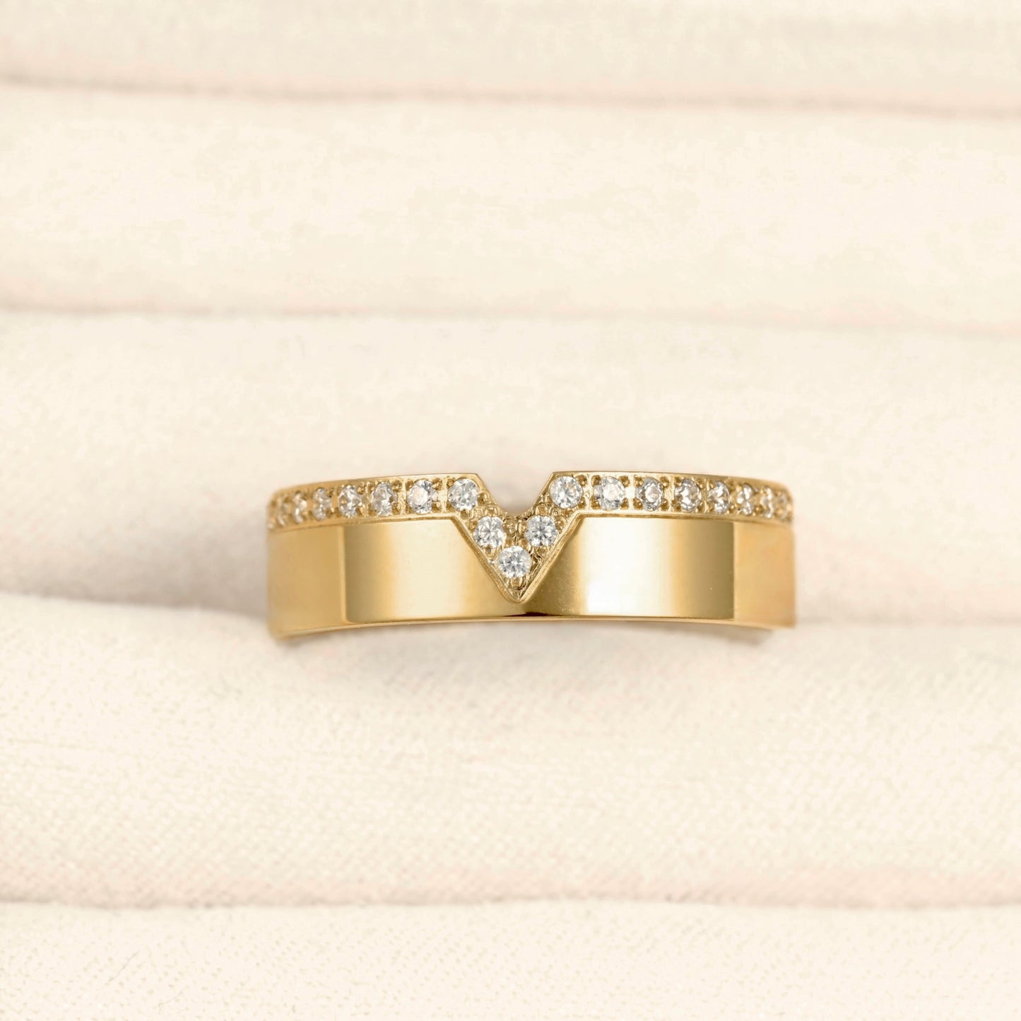 A yellow gold ring with a V-shaped pavé diamond band, displayed on a textured cream-colored ring box.