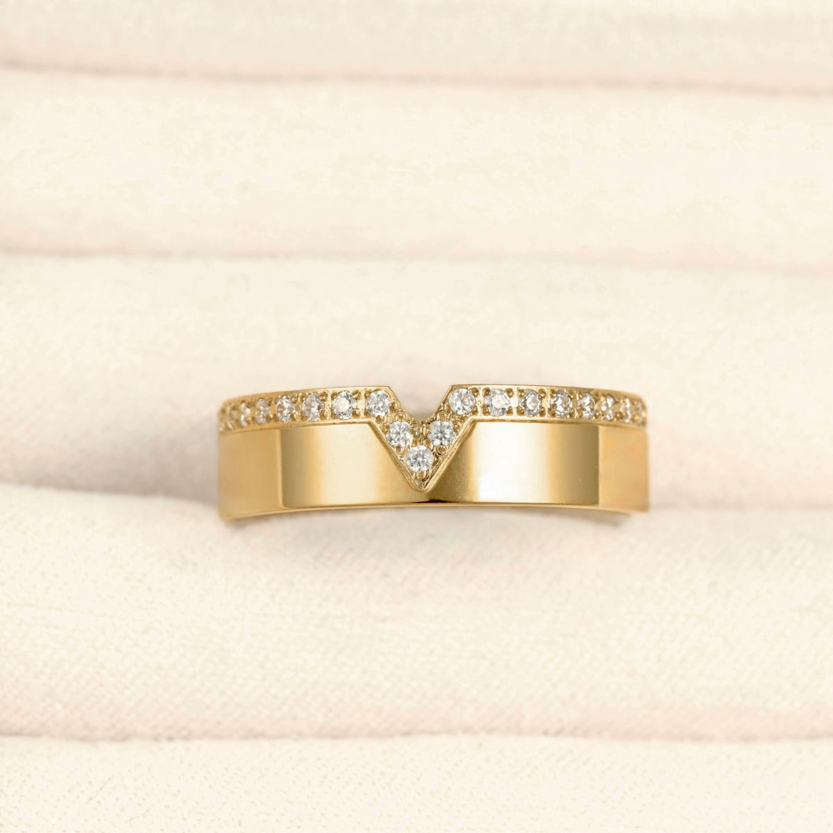A yellow gold ring with a V-shaped pavé diamond band, displayed on a textured cream-colored ring box.