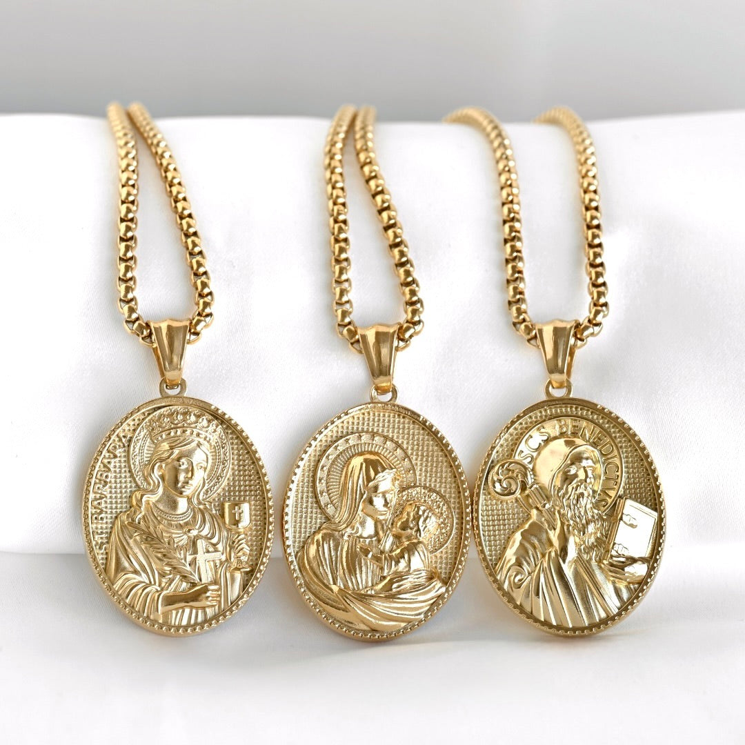 Three gold-plated oval religious medallion necklaces with detailed engravings, displayed on a white fabric stand.