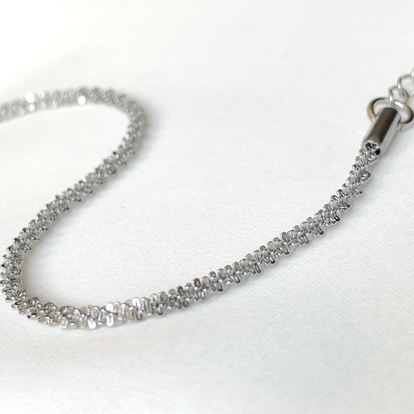 Close-up view of dainty sparkly silver chain bracelet on a white background