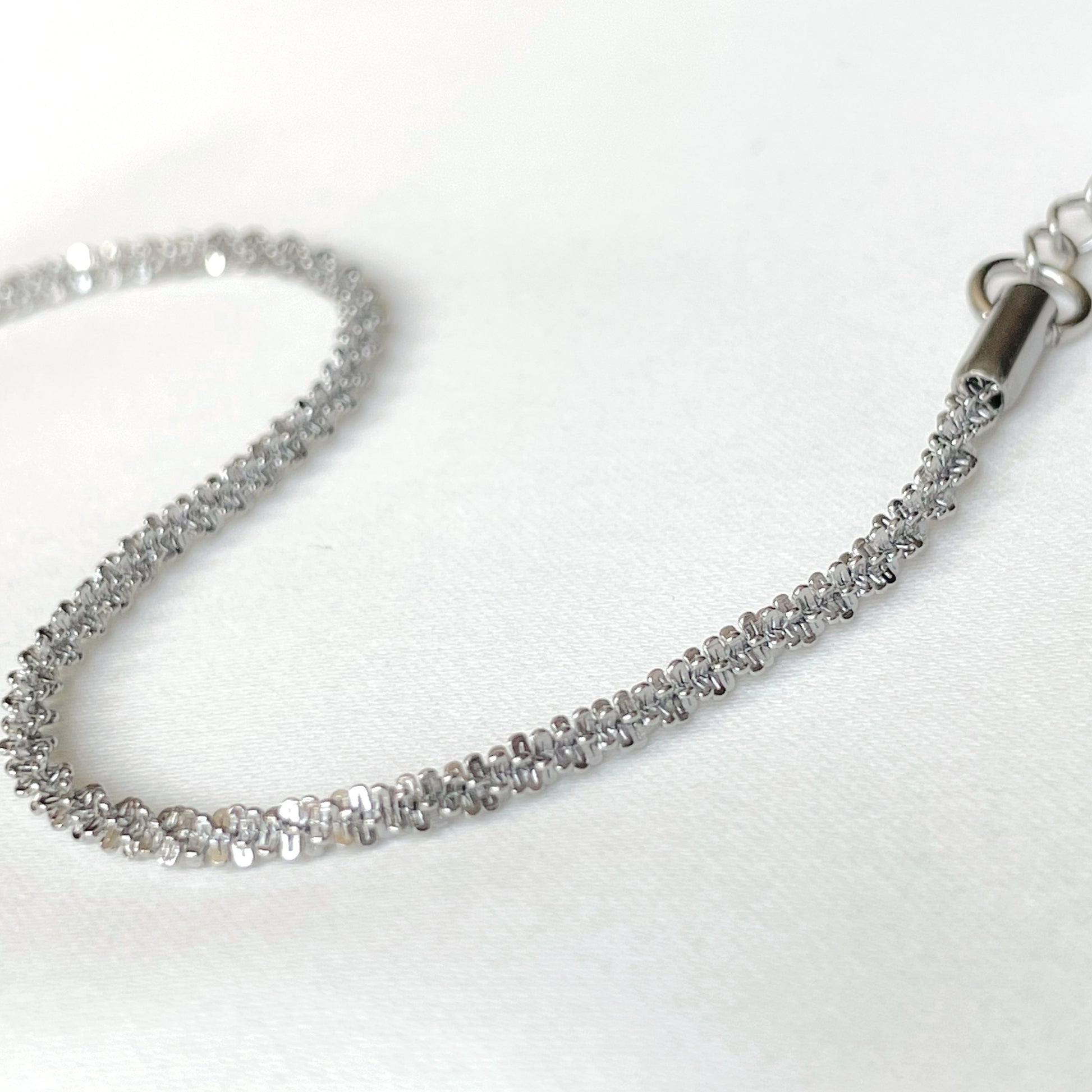 Close-up view of dainty sparkly silver chain bracelet on a white background