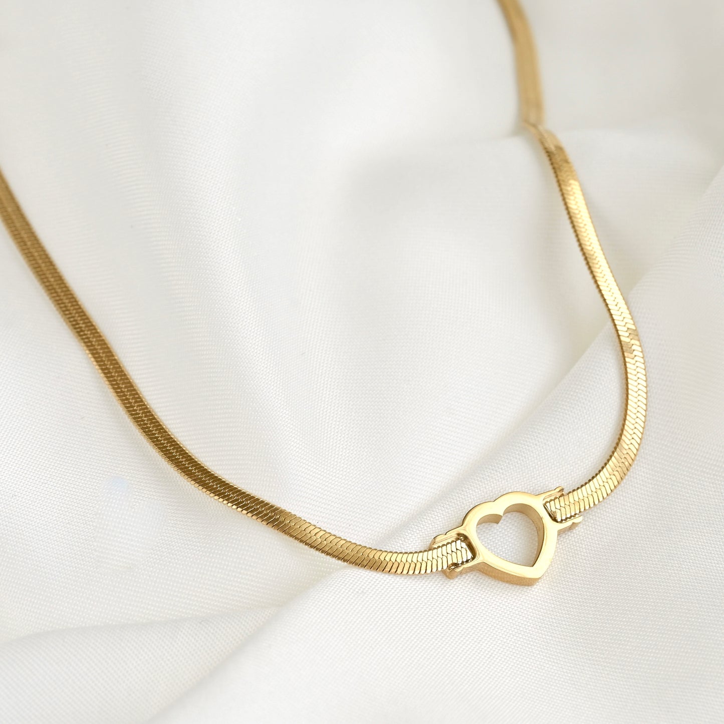 Gold flat snake chain necklace with a heart charm on a white background