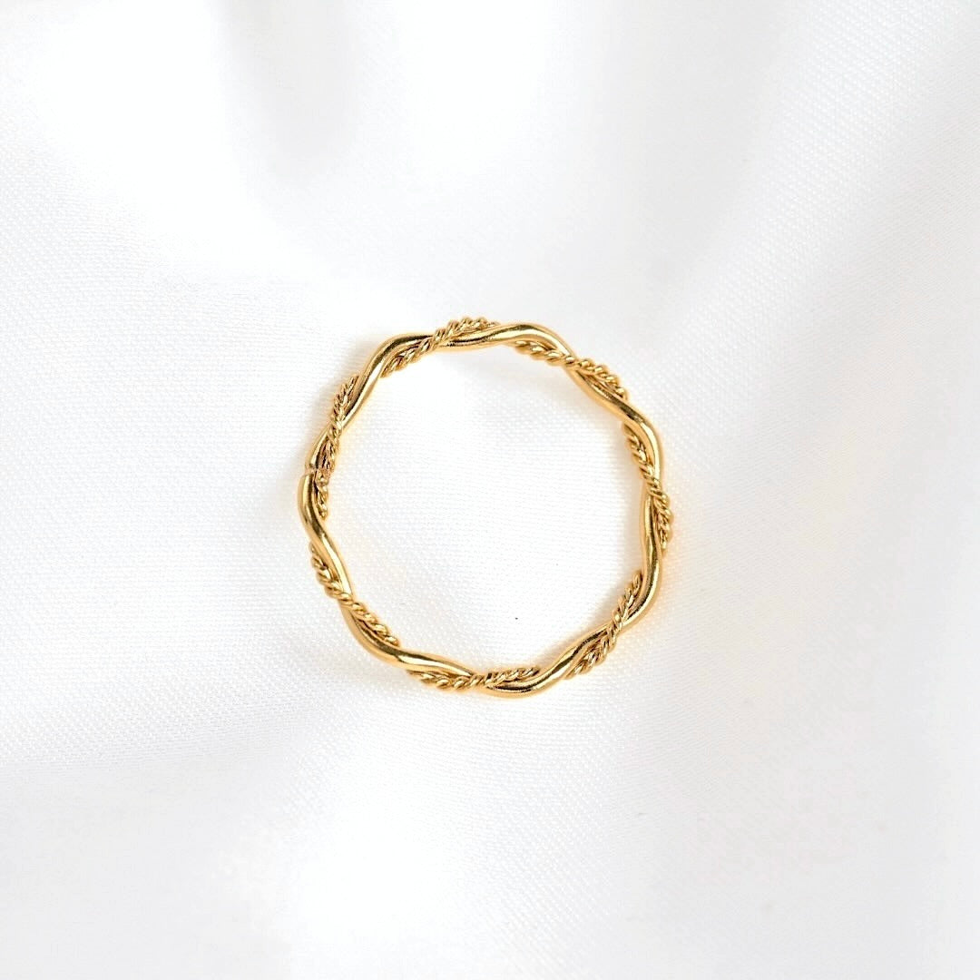 A thin gold twisted rope ring, also known as a cable or spiral ring, displayed on a textured white fabric background.