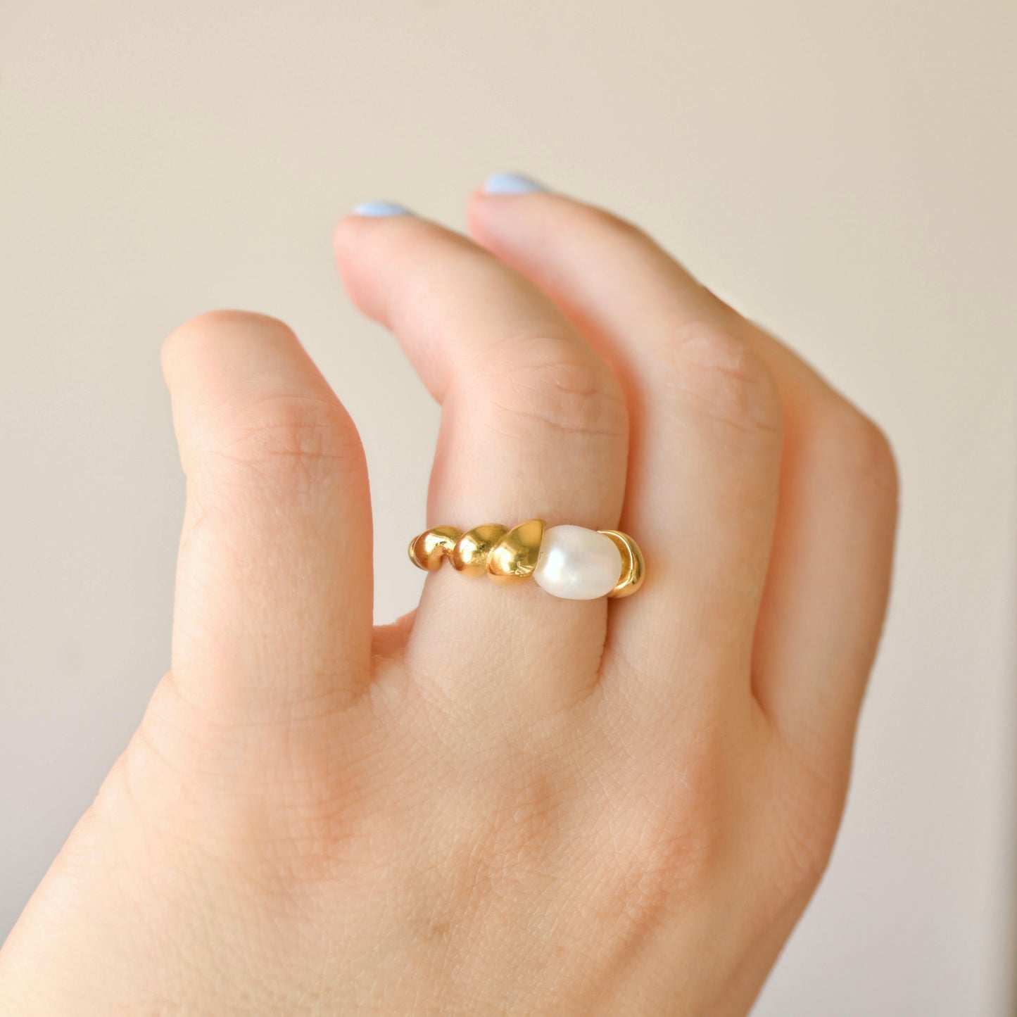 Gold twisted croissant ring with a medium sized pearl on a hand against a neutral background