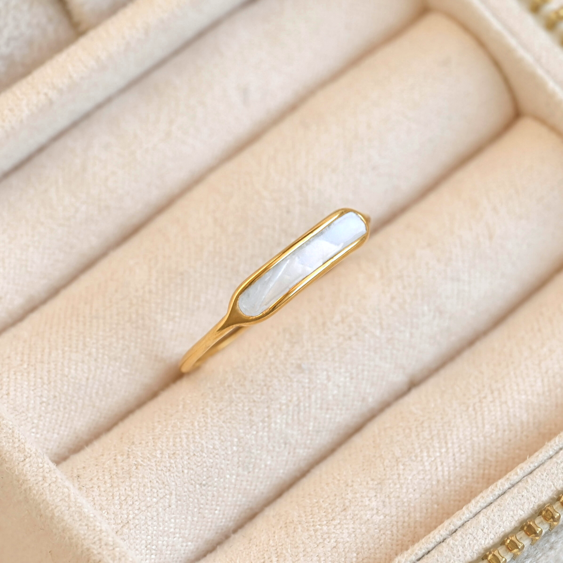 Gold  mother of pearl ring with a white shell bar on a beige fabric surface