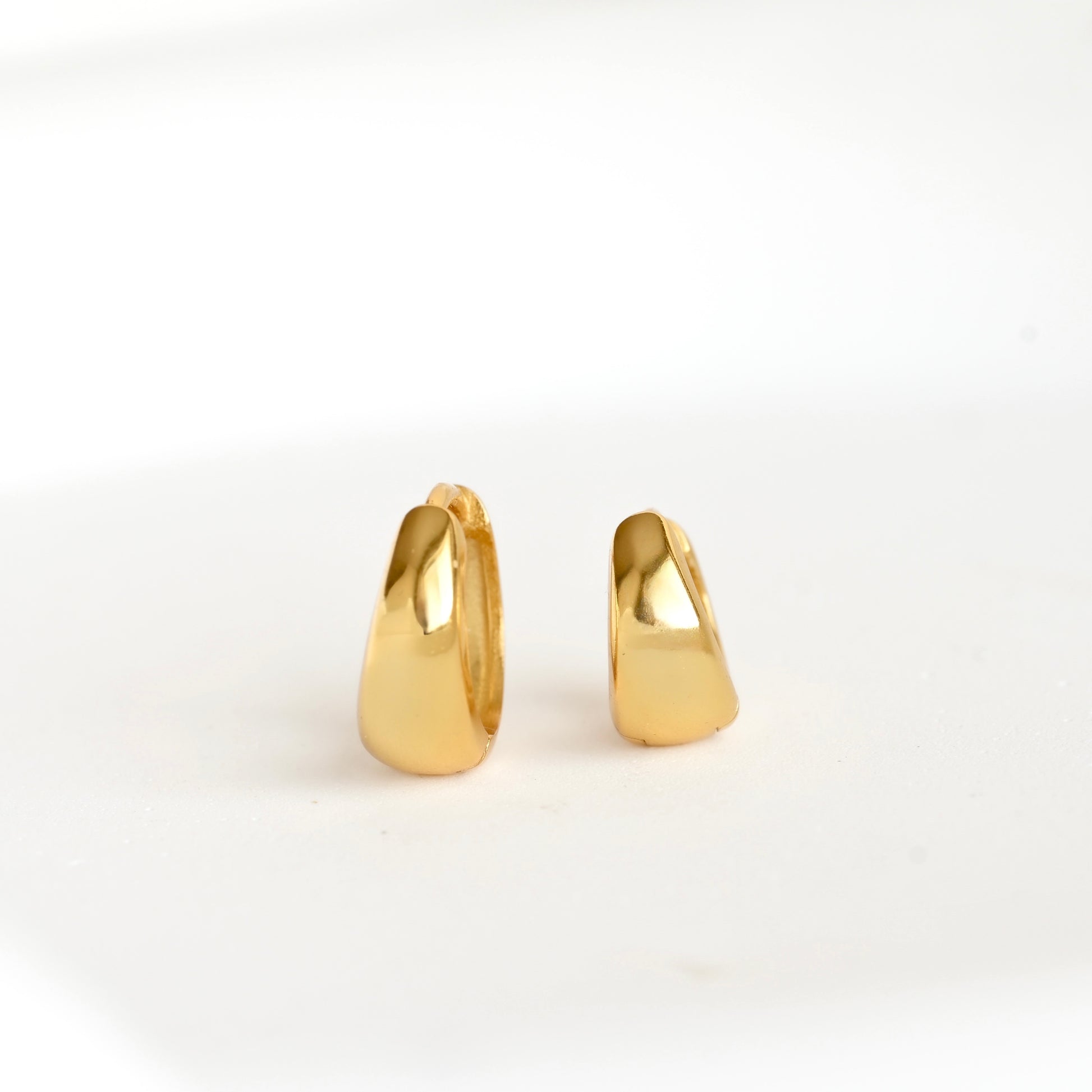 Front view of tapered gold huggie earrings in two different sizes on a white background