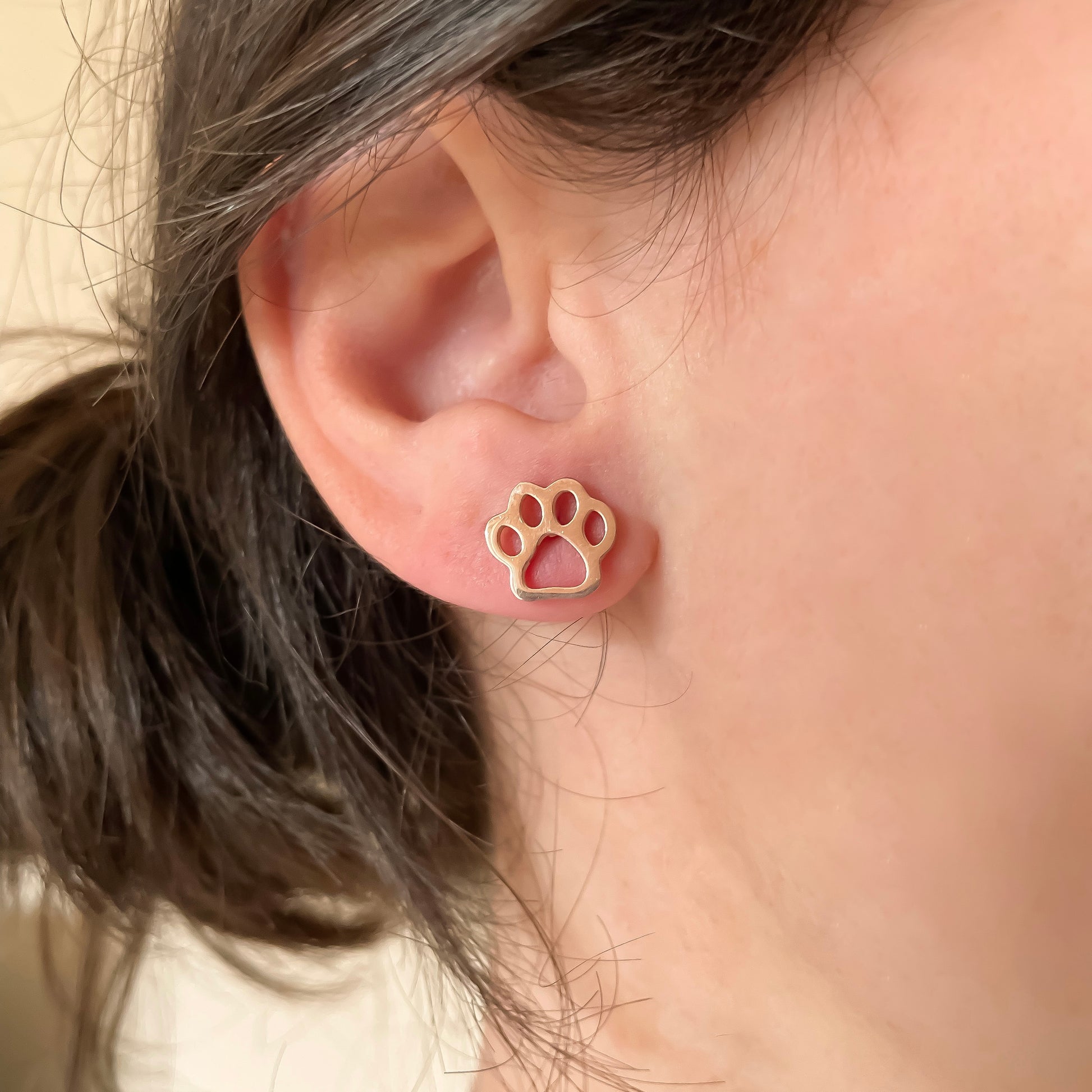 Rose gold paw print stud earrings worn by a person with a neutral background
