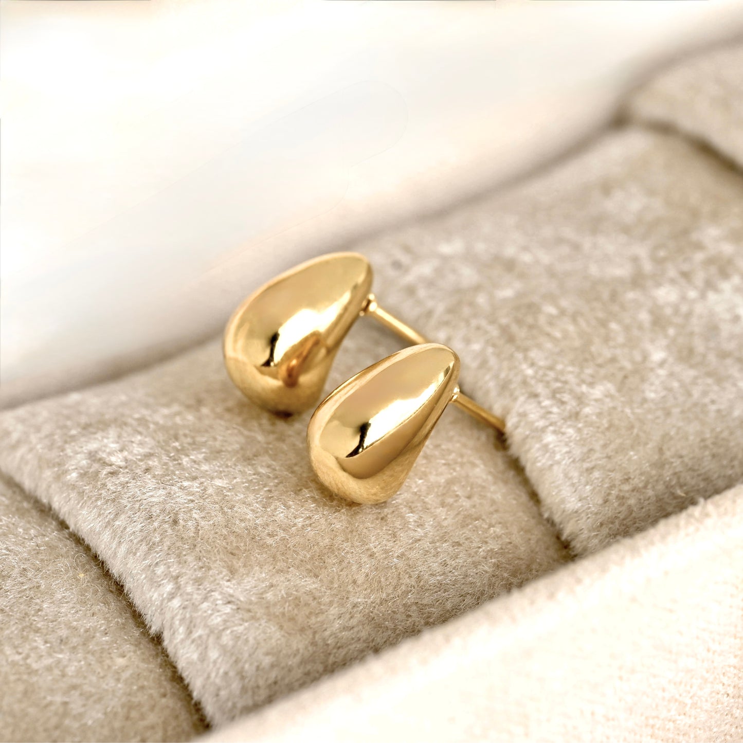 Bold Gold huggie earrings on a soft fabric surface