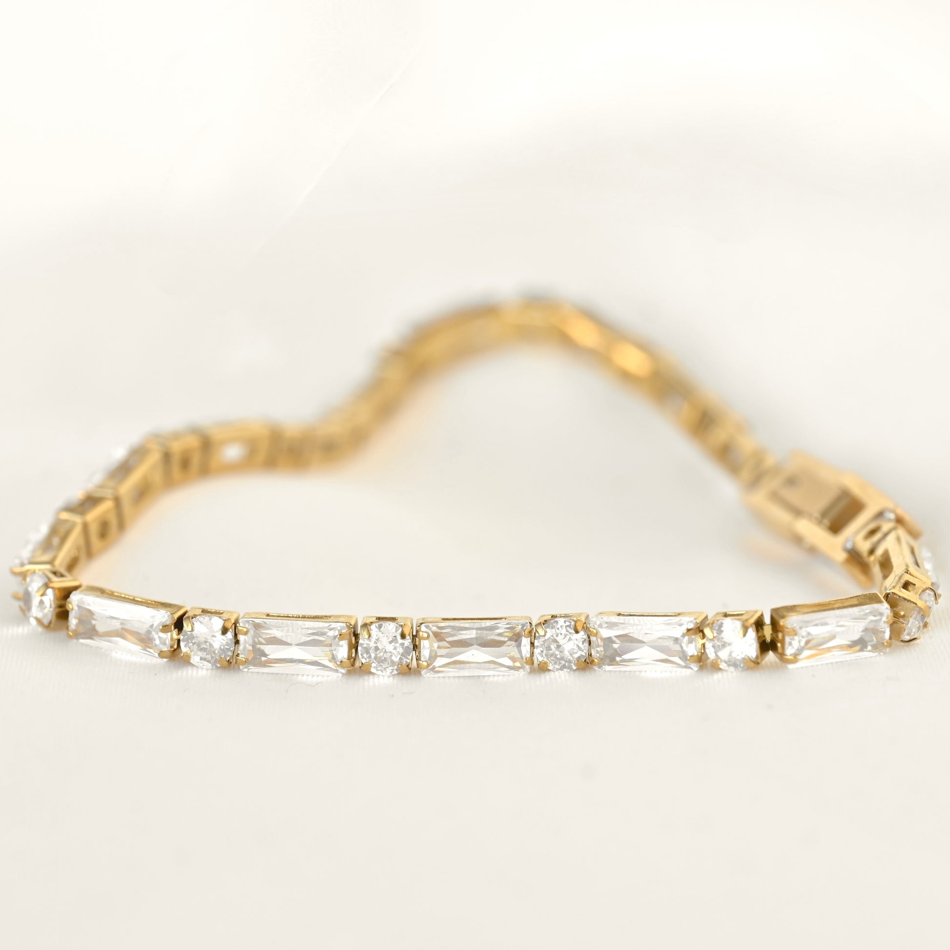 A yellow gold tennis bracelet featuring a row of clear round and  baguette-cut CZ stones, displayed on a clean white background.