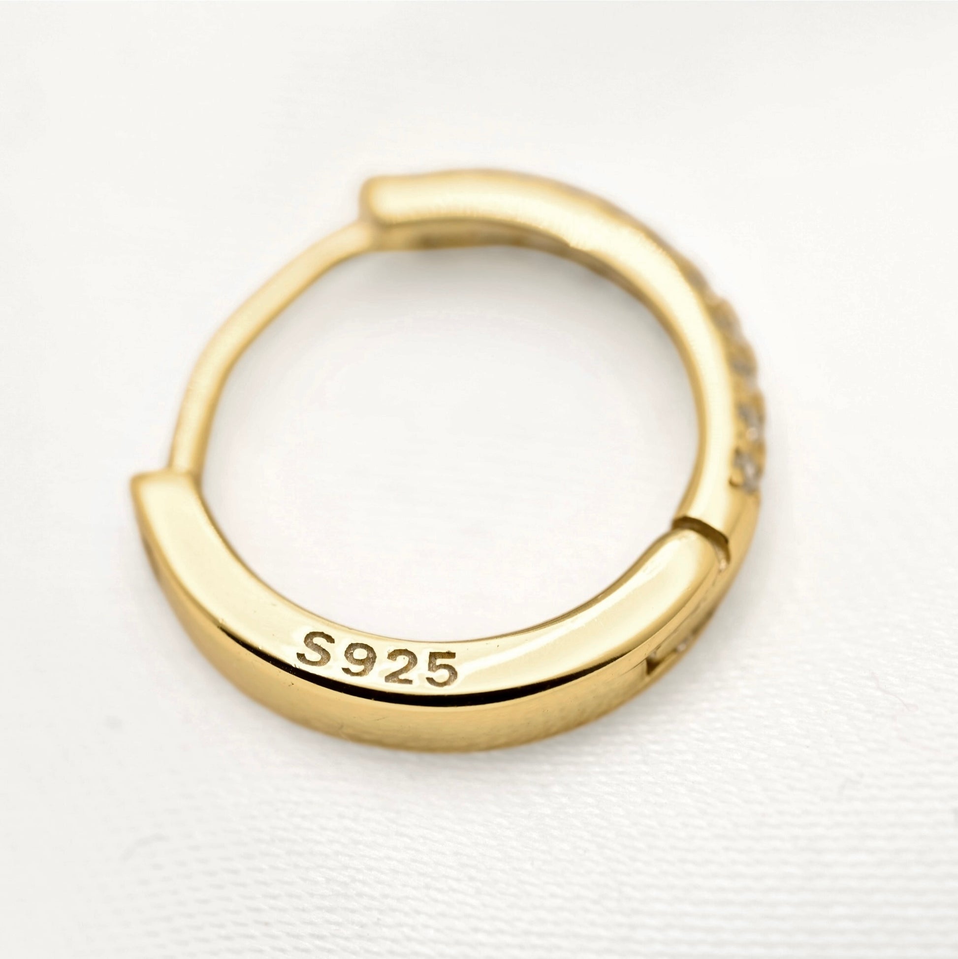 A gold huggie hoop ring with 'S925' sterling silver purity stamped on the inside, shown on a textured white background.