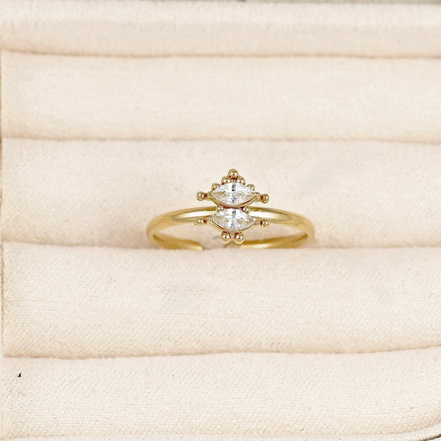 A gold ring with a marquise-cut diamond center and small accent diamonds, displayed on a cream-colored velvet ring box.