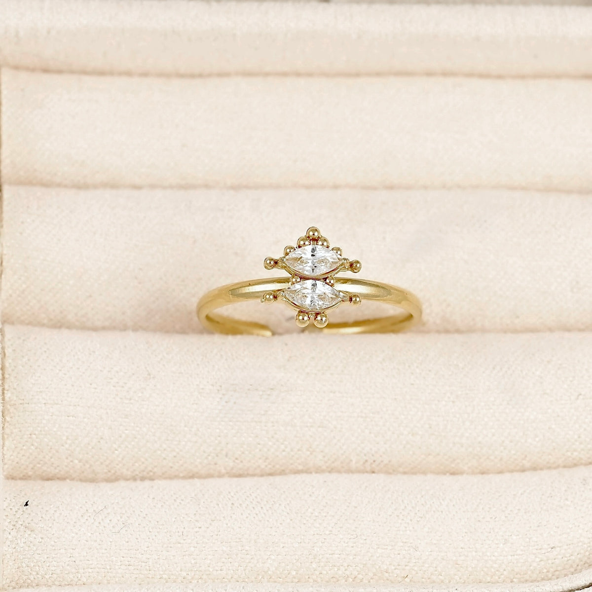 A gold ring with a marquise-cut diamond center and small accent diamonds, displayed on a cream-colored velvet ring box.