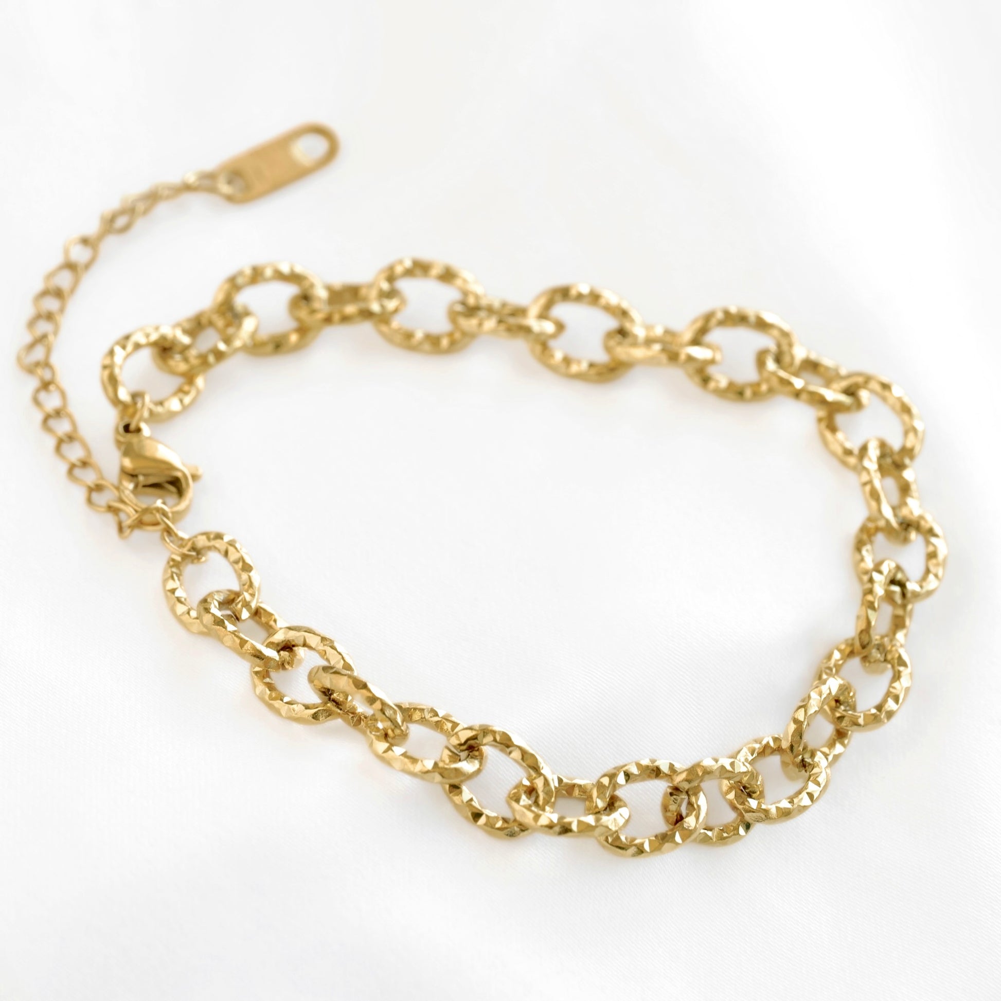 A gold chain bracelet with textured oval links and an adjustable lobster clasp, displayed on a clean white background.