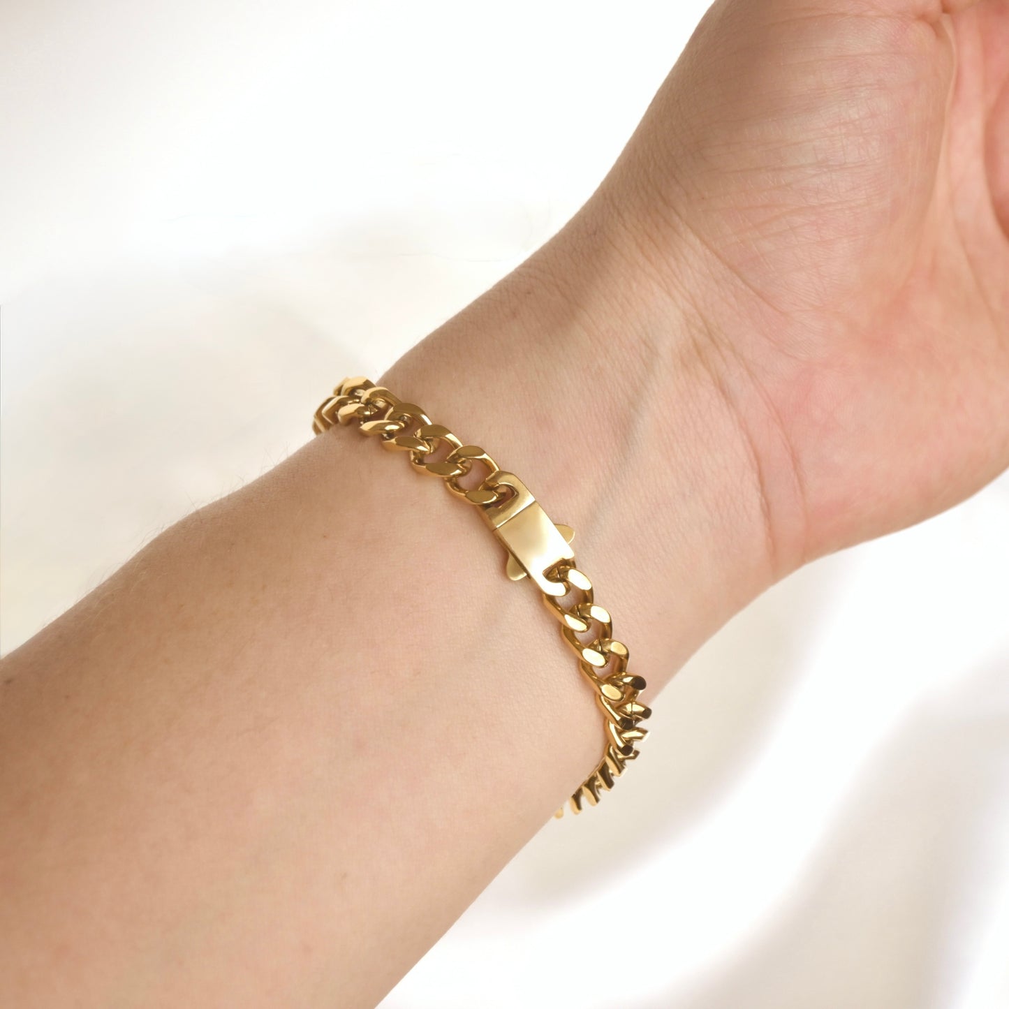 A gold-toned chunky curb link bracelet worn on a person's wrist, shown against a bright white background.
