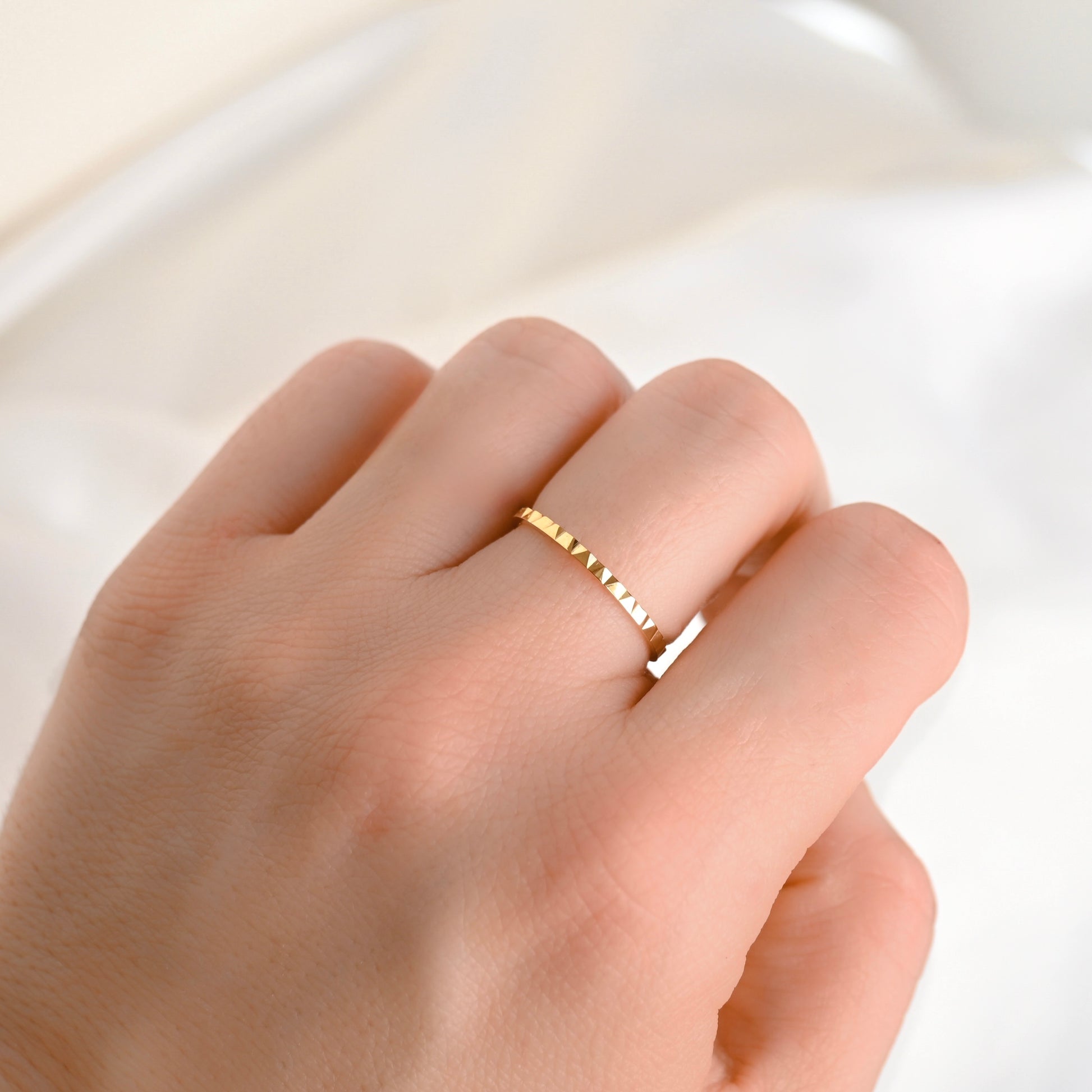 Thin gold geometric ring on a person's finger against a white background