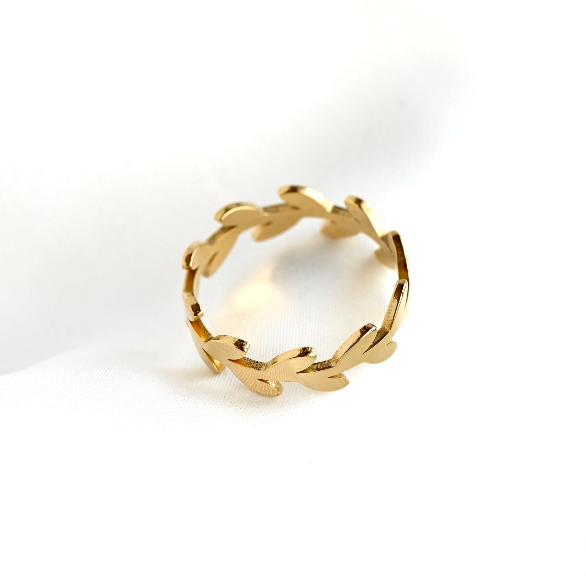 Top view of a gold leaf-patterned band ring resting on a white textured surface.