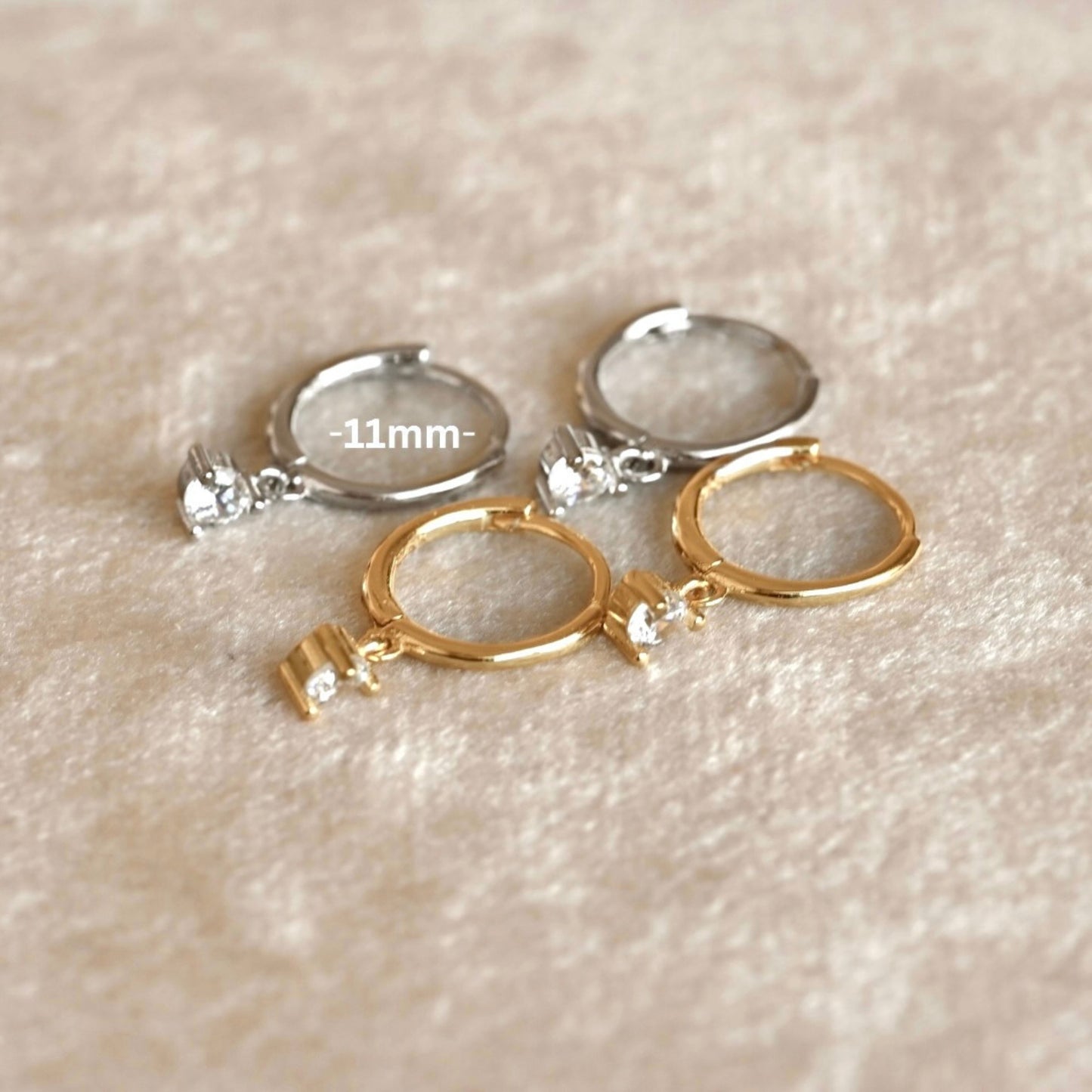 Gold and silver hoop earrings with CZ charms on a beige textured background