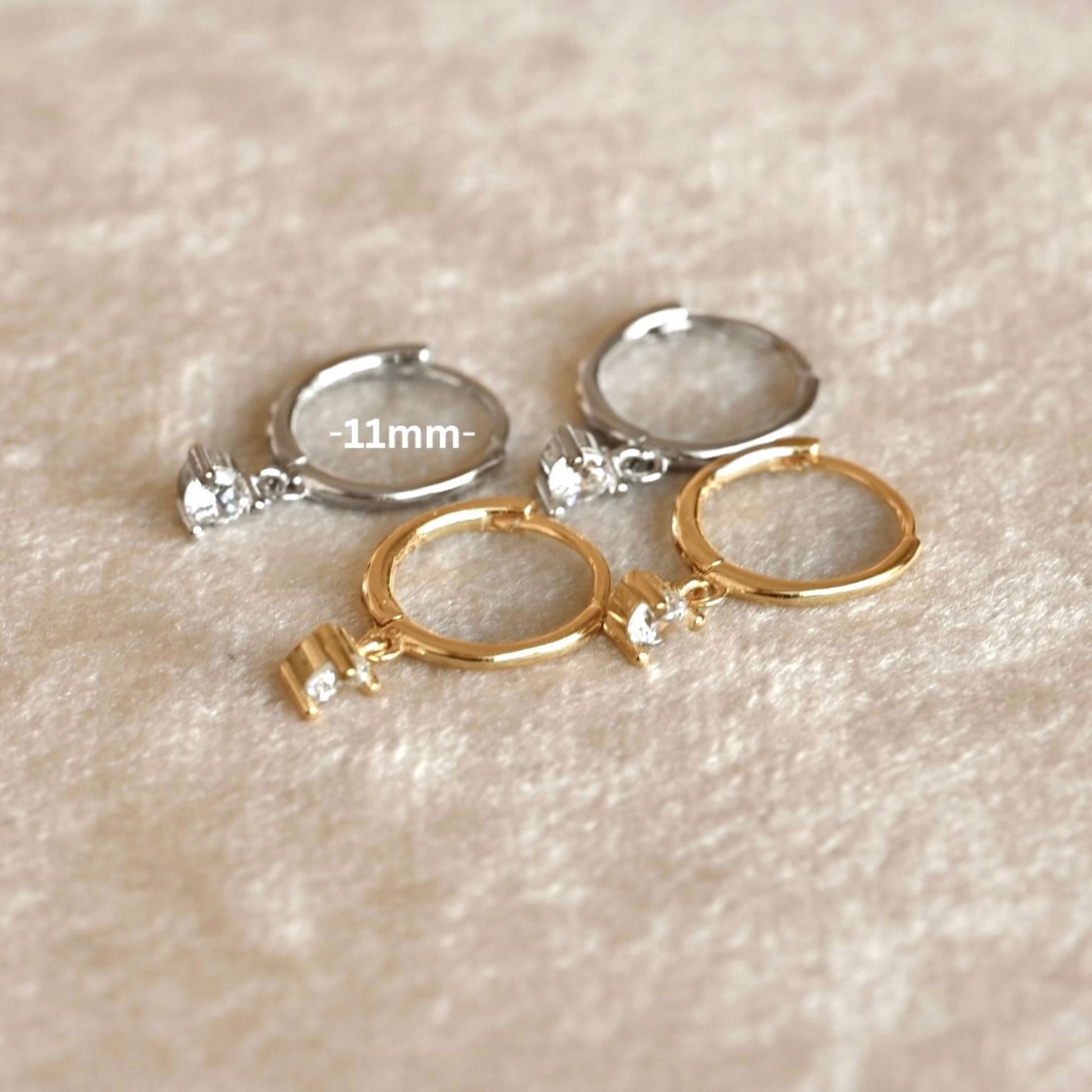 Gold and silver hoop earrings with CZ charms on a beige textured background