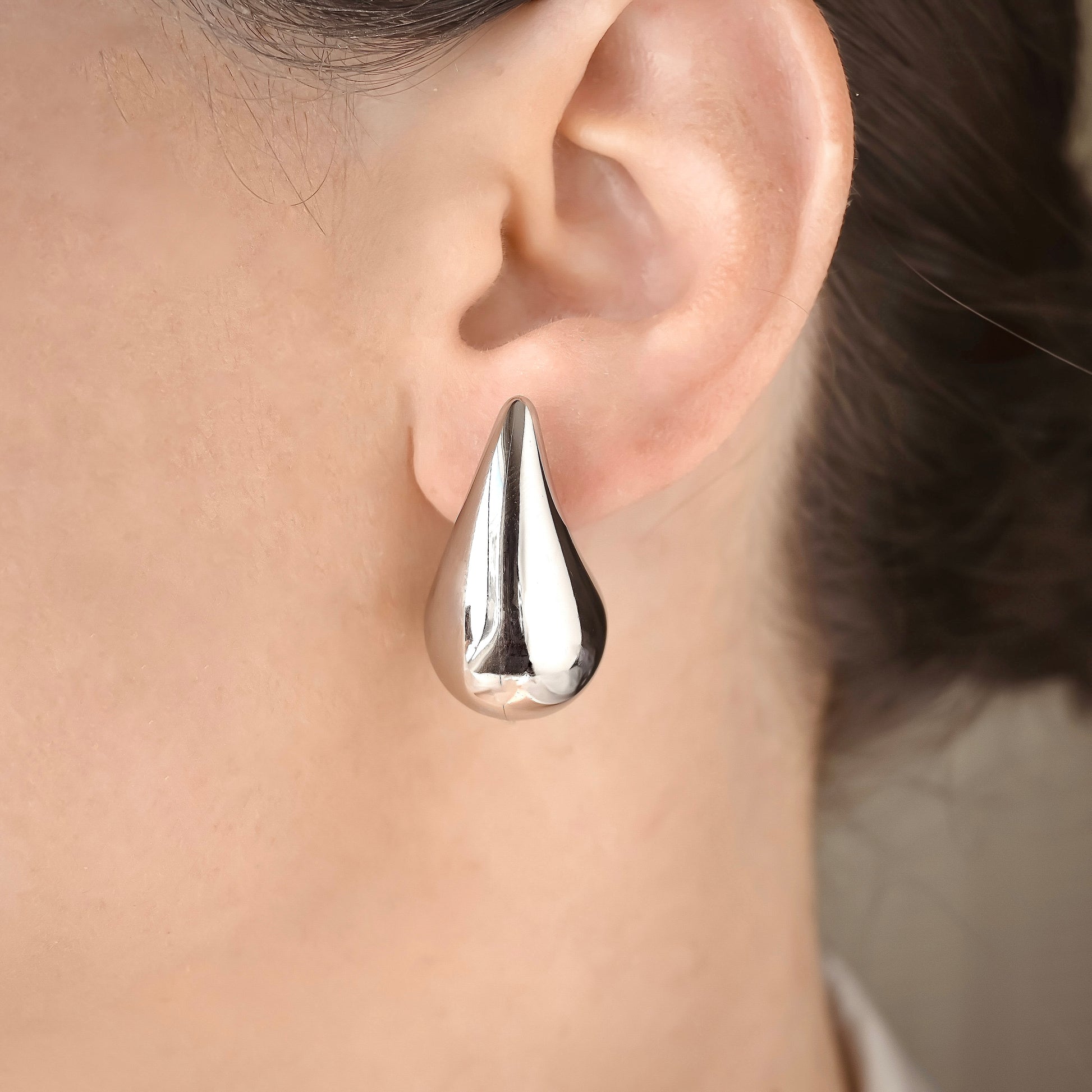 Chunky silver teardrop earring worn on a person's ear with a neutral background