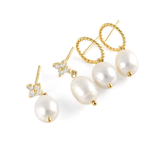 A pair of gold-plated drop earrings with large white baroque pearls, one featuring a twisted hoop and the other a flower-shaped cluster of clear crystals, shown on a white background.