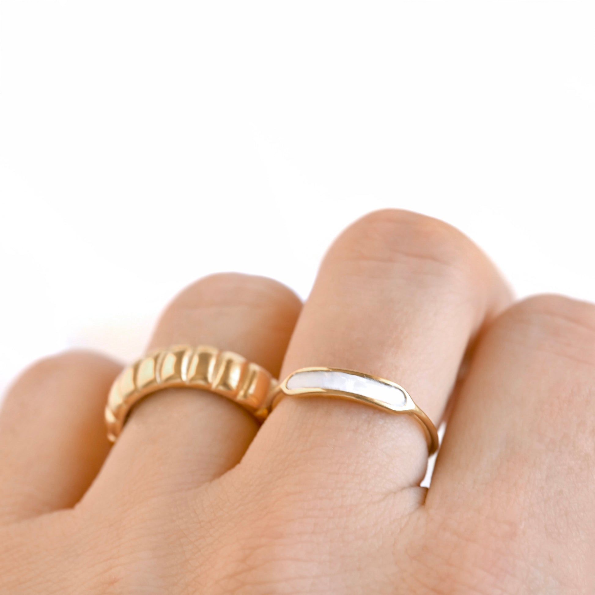 Gold shell pearl ring on a finger against a white background