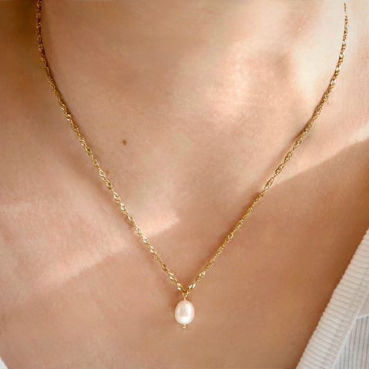 A delicate gold singapore chain necklace with a single small white pearl pendant, worn on a person's neck.