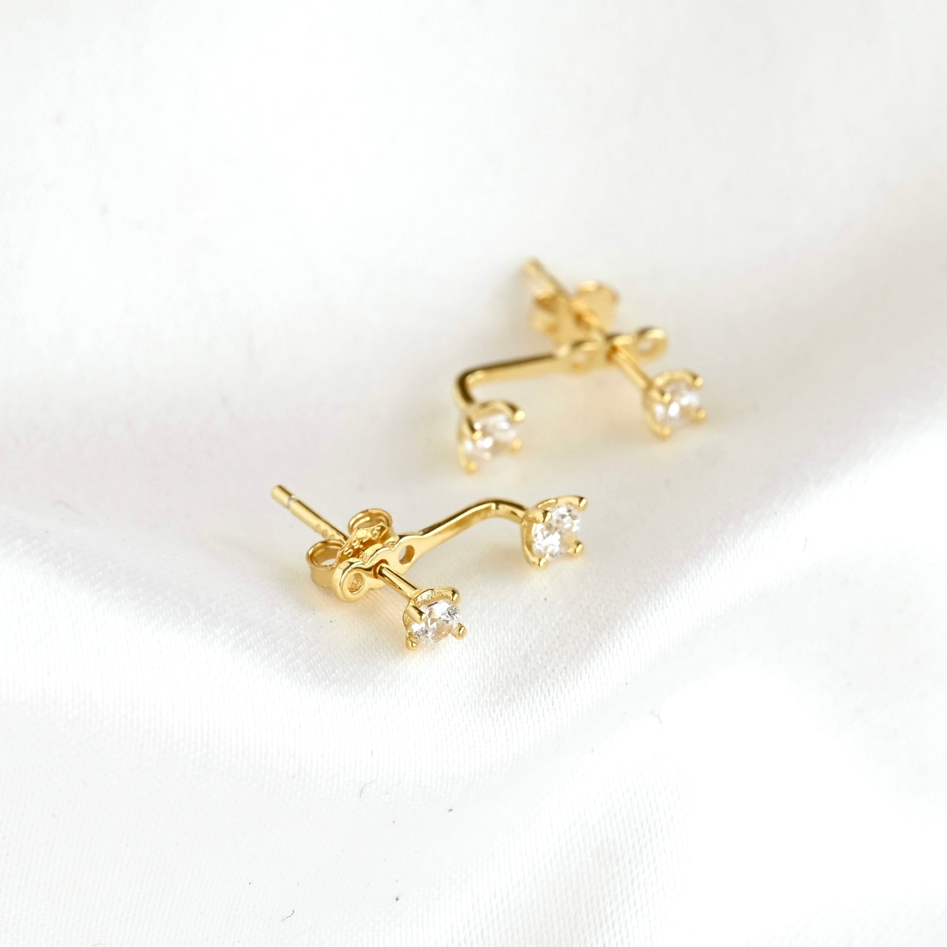 A pair of gold ear jacket with two small round clear diamonds on  a white backgorund