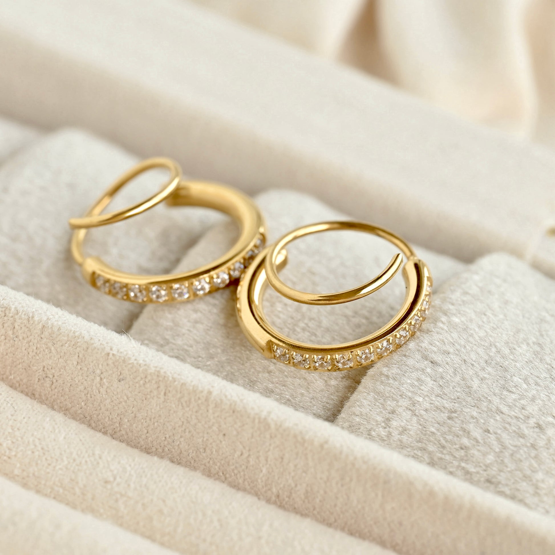 A pair of gold twist hoop earrings with small clear stones set along the front, displayed on a cream-colored jewelry box.