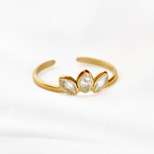 A gold adjustable ring featuring three marquise-cut clear gemstones in a row, displayed on a soft white fabric background.