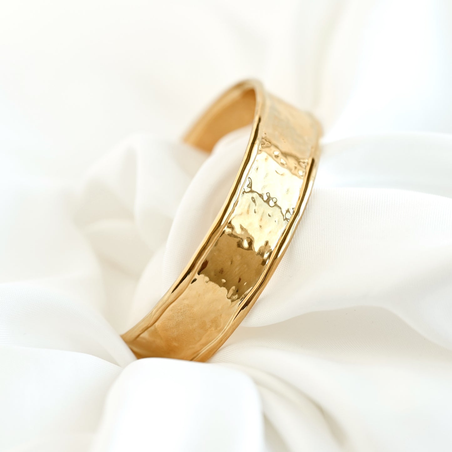Wide Gold cuff bracelet with a hammered design on a white fabric background
