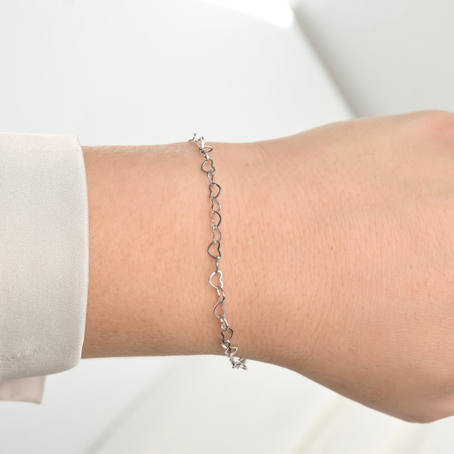 Silver heart-shaped bracelet on a wrist with a plain background