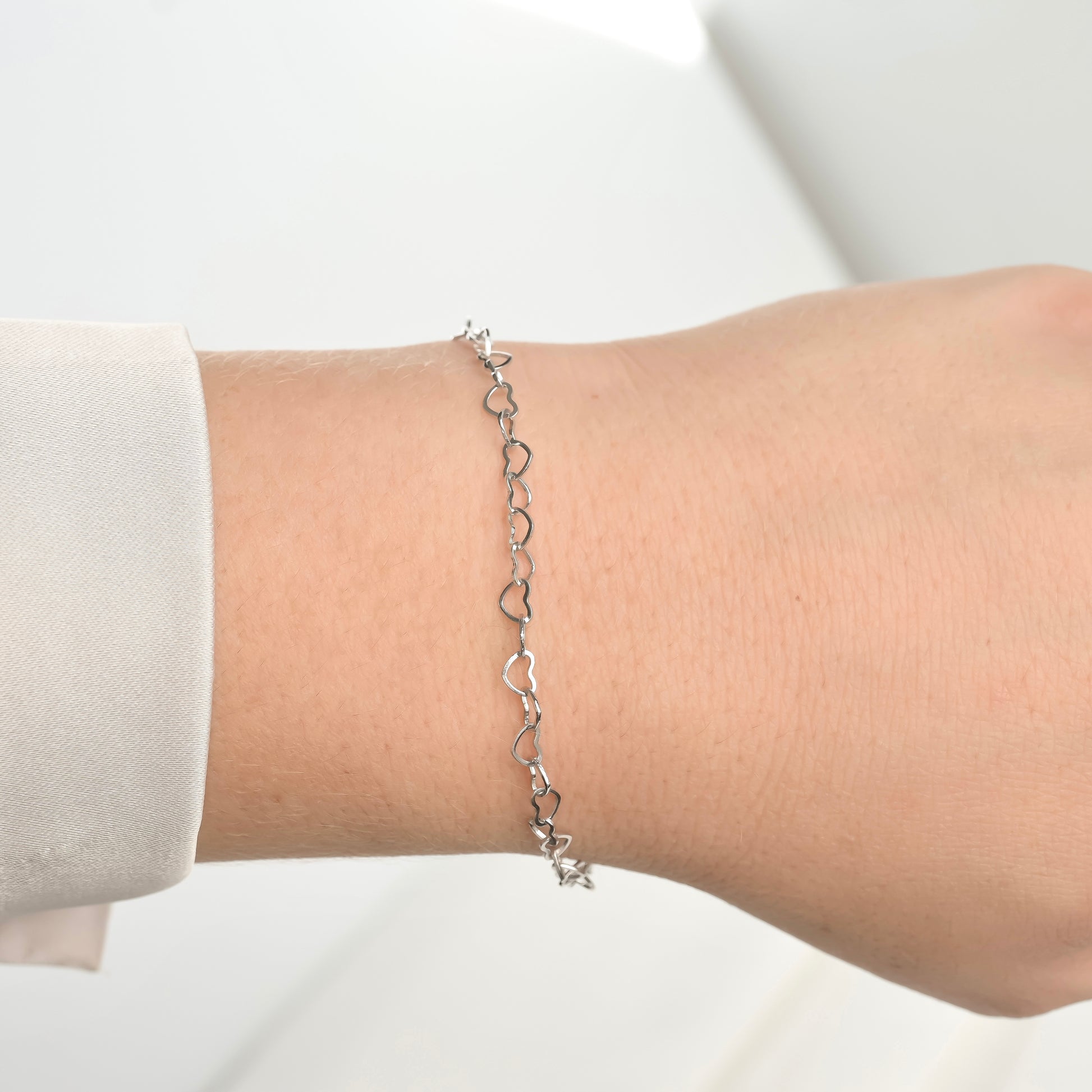 Silver heart-shaped bracelet on a wrist with a plain background