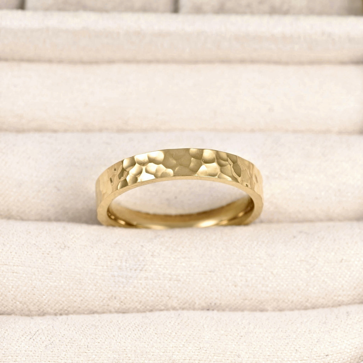 A hammered gold band ring resting on a textured beige fabric surface.