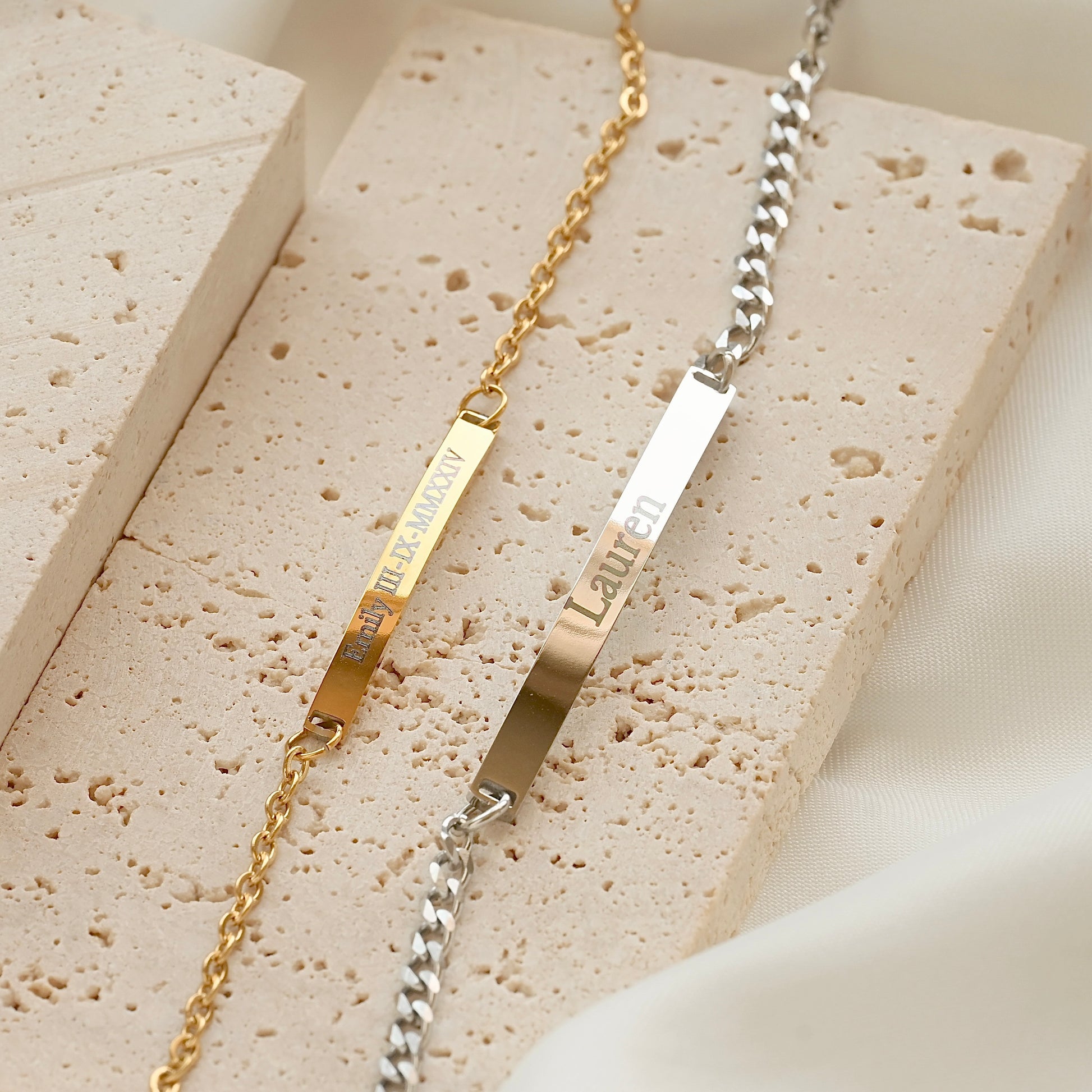Two gold and silver bar bracelets on a textured stone surface