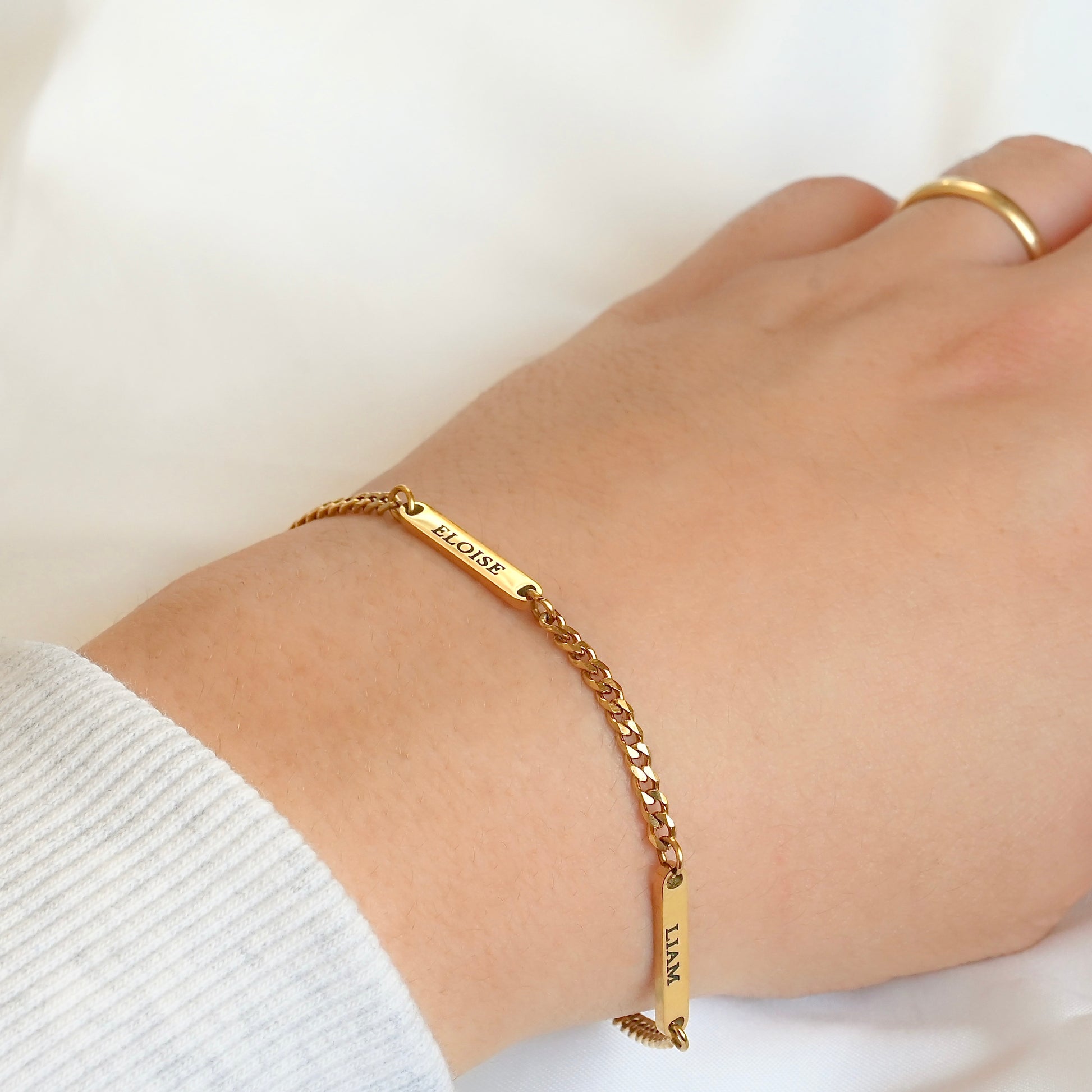 Gold curb bracelet with engraved text on a wrist against a white background