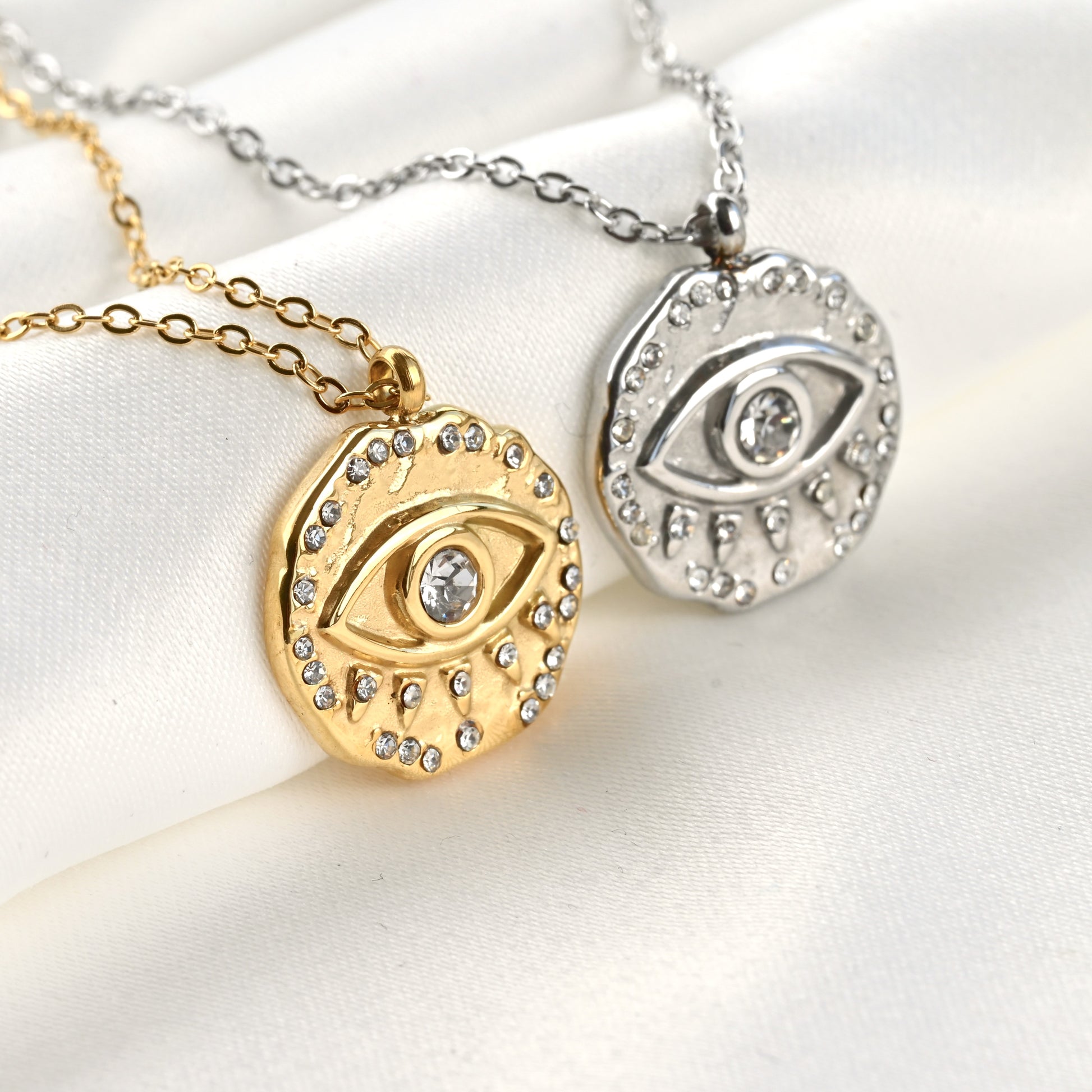 Two eye-shaped pendants on gold and silver chains against a white background