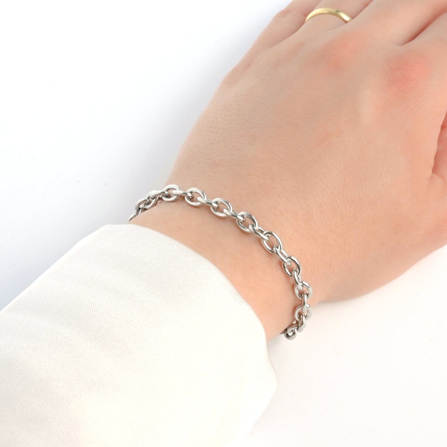 Thick Silver rolo chain bracelet on a wrist with a plain background