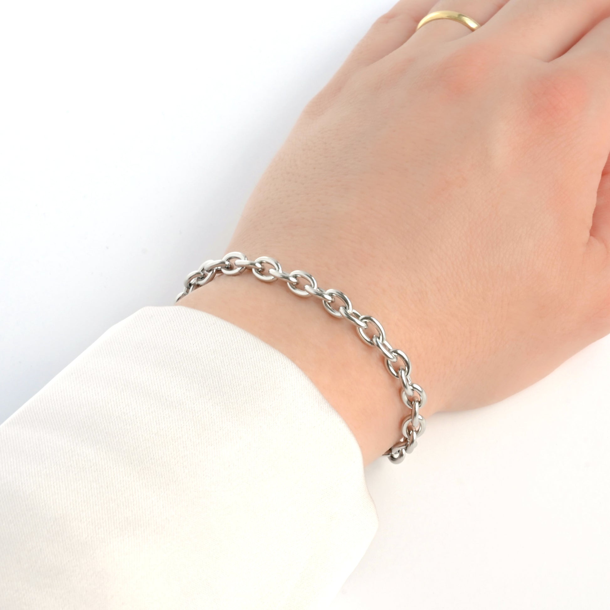 Thick Silver rolo chain bracelet on a wrist with a plain background