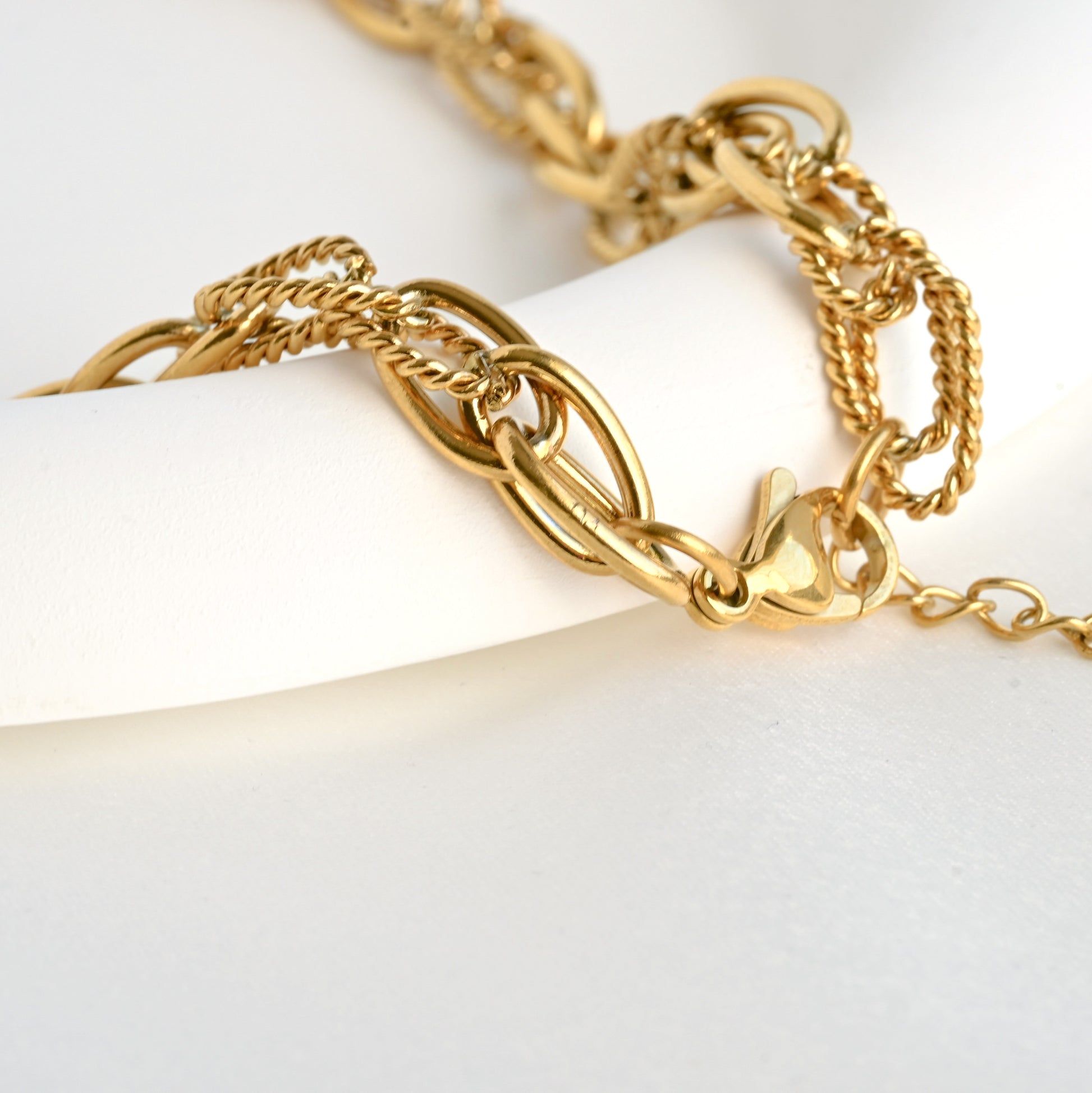 Close up of the clasp area of Gold mixed chain necklace  with a lobster clasp and extender, on a white plate