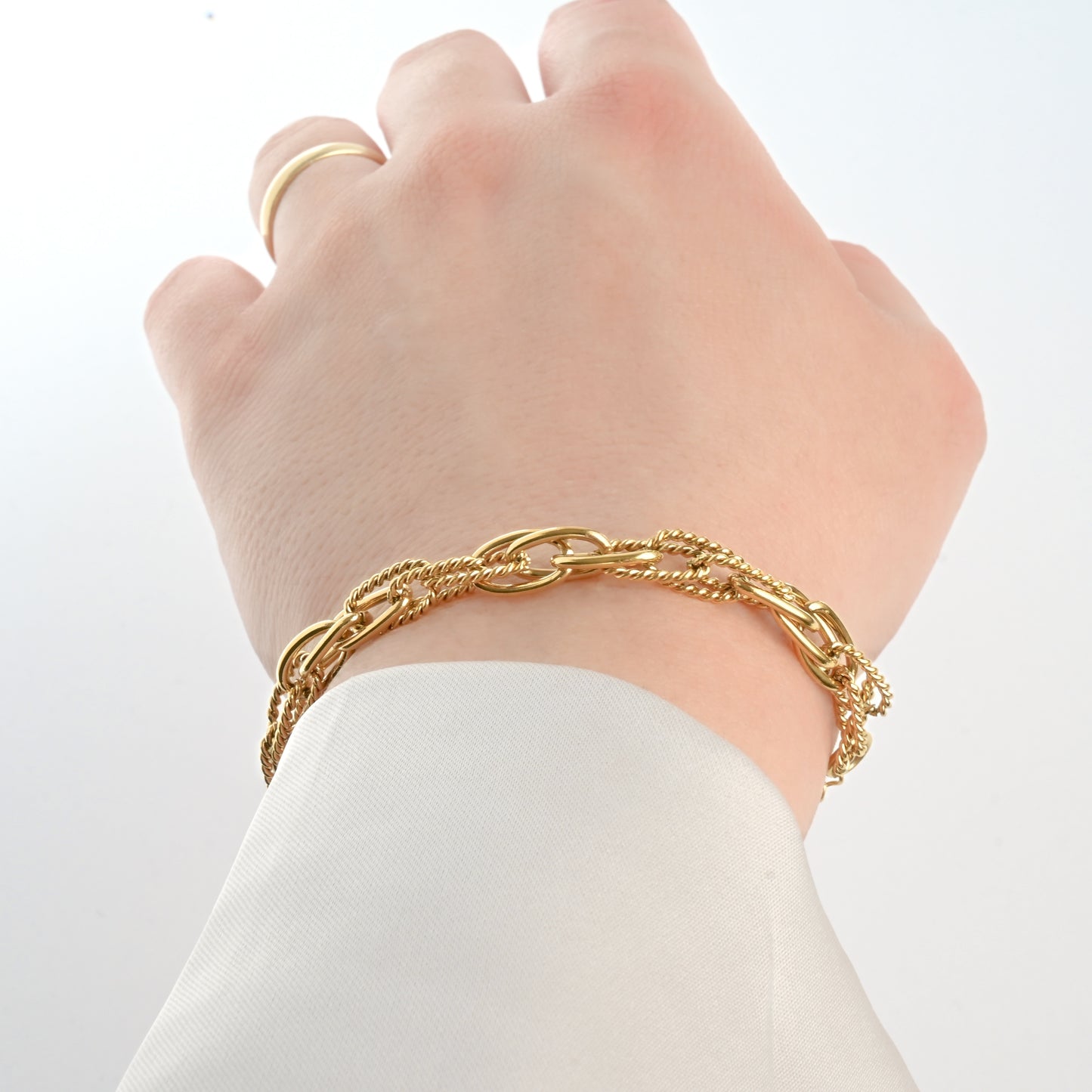 Thick gold bracelets on a wrist with a plain background