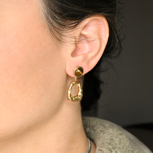 Close-up of a person wearing  hammered gold drop earrings with a blurred background