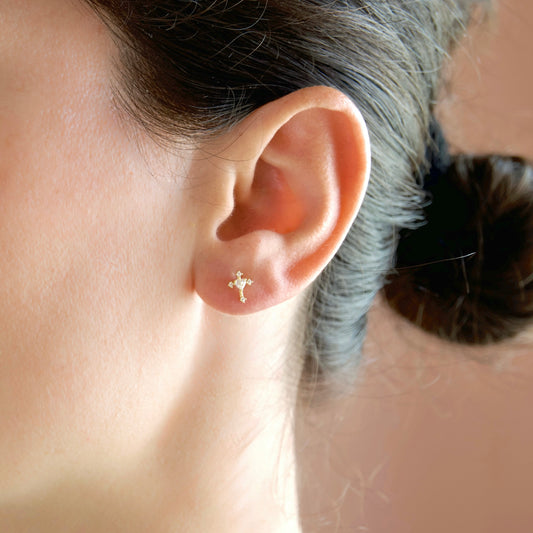 A close-up of a person's ear wearing a tiny gold cross stud earring.