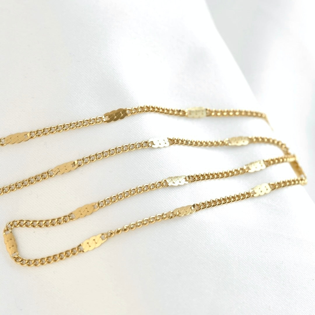 A delicate gold chain necklace with flat, polished rectangular links, displayed on a soft white fabric background.