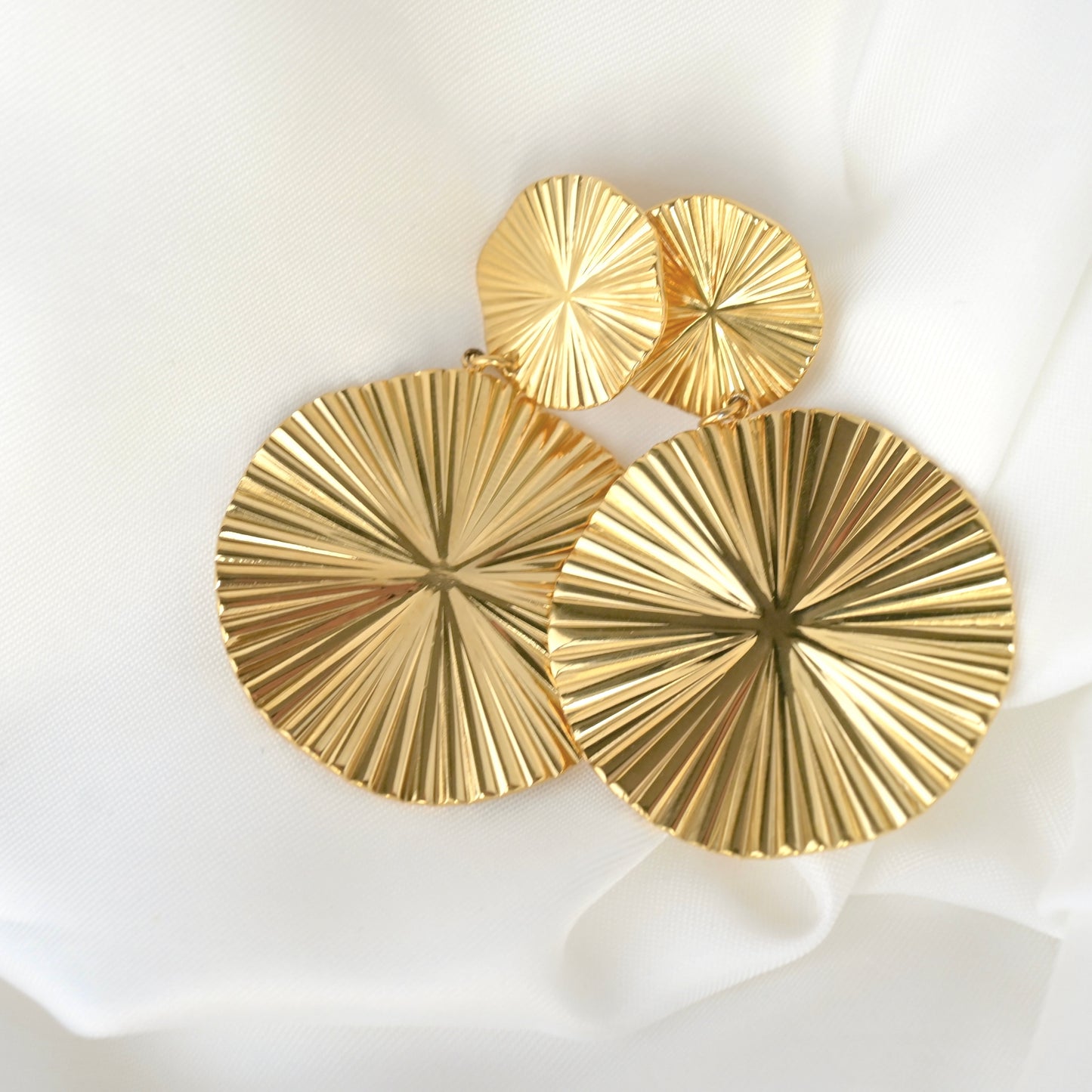 Gold earrings with a textured organic design on a white background