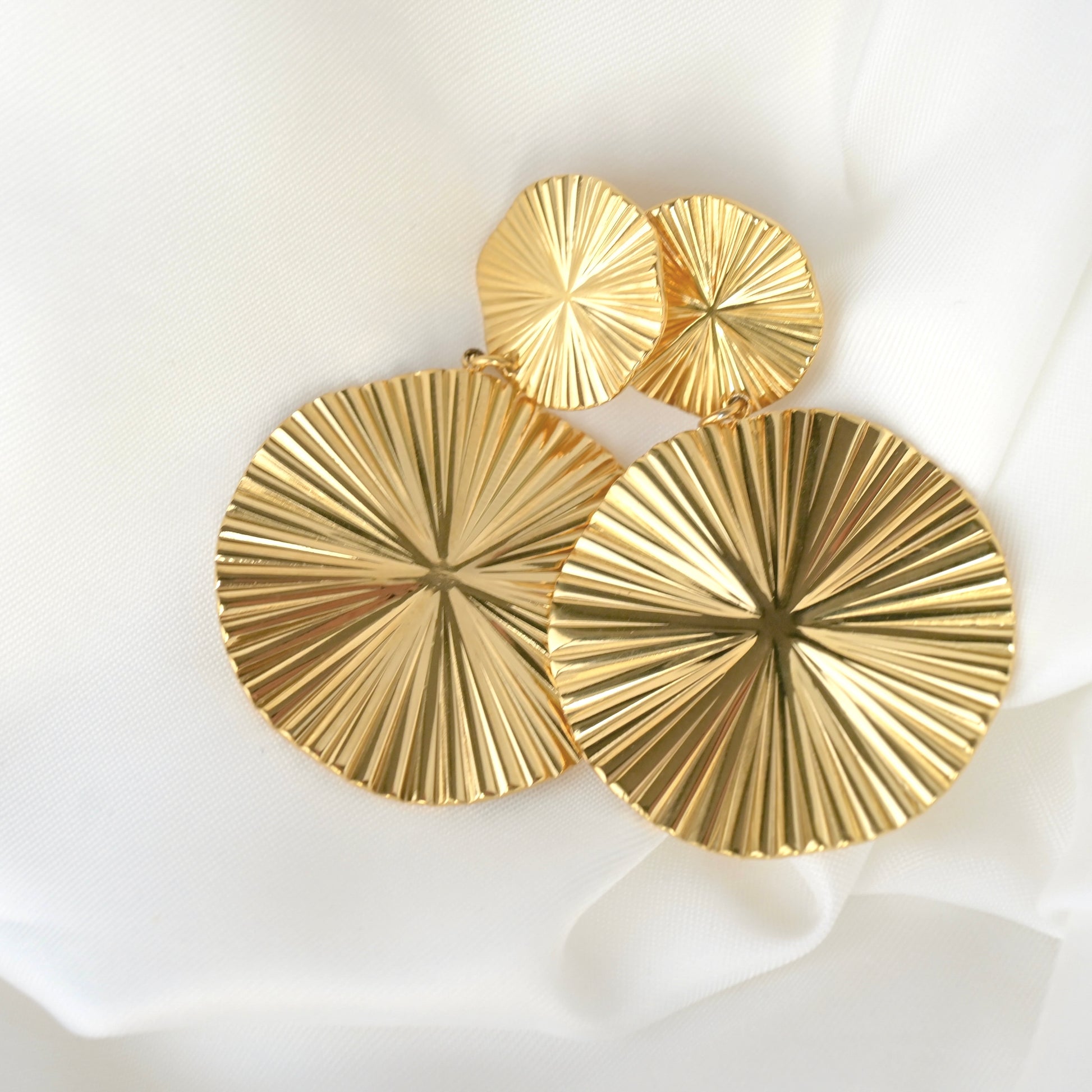 Gold earrings with a textured organic design on a white background