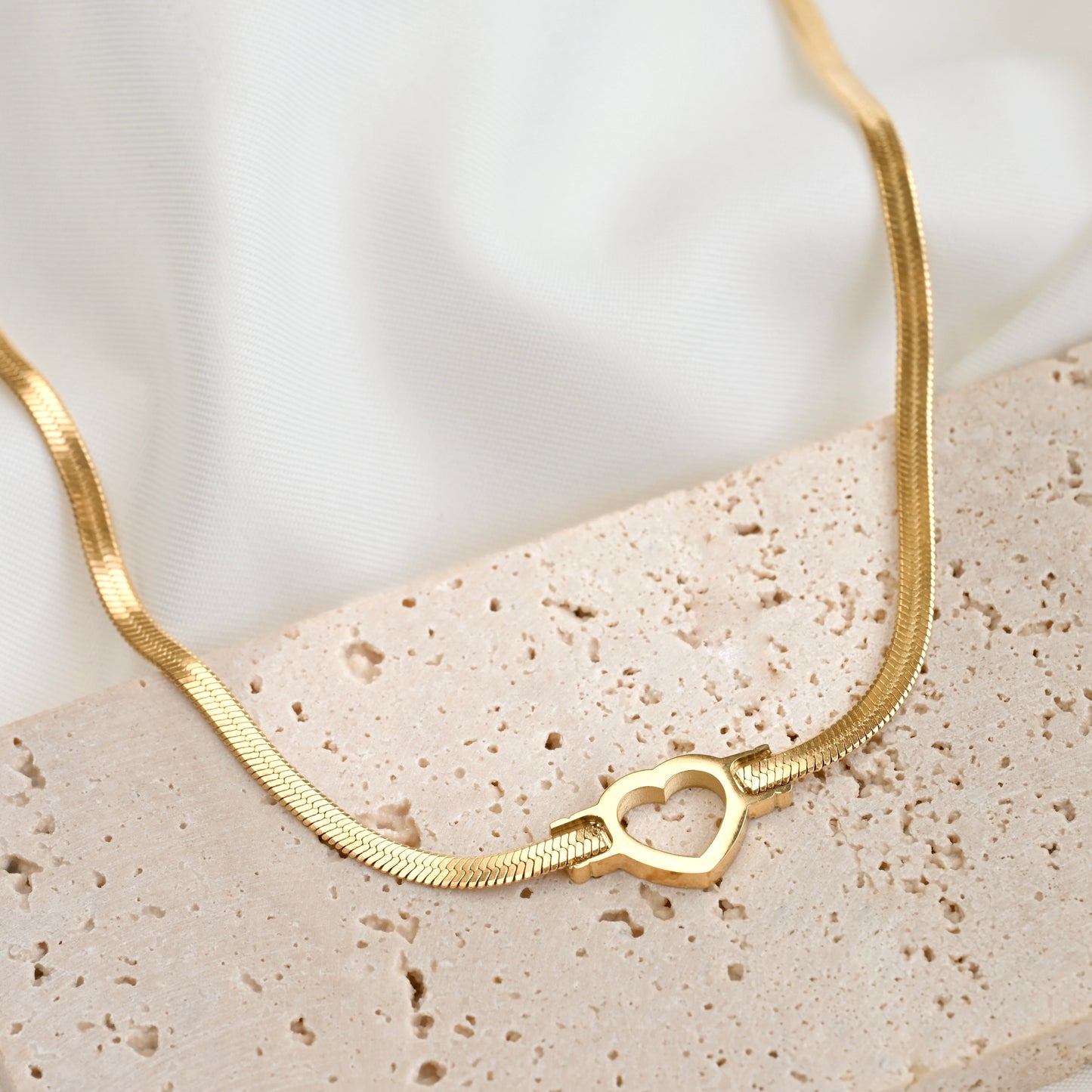 18k Gold heart necklace on a textured surface