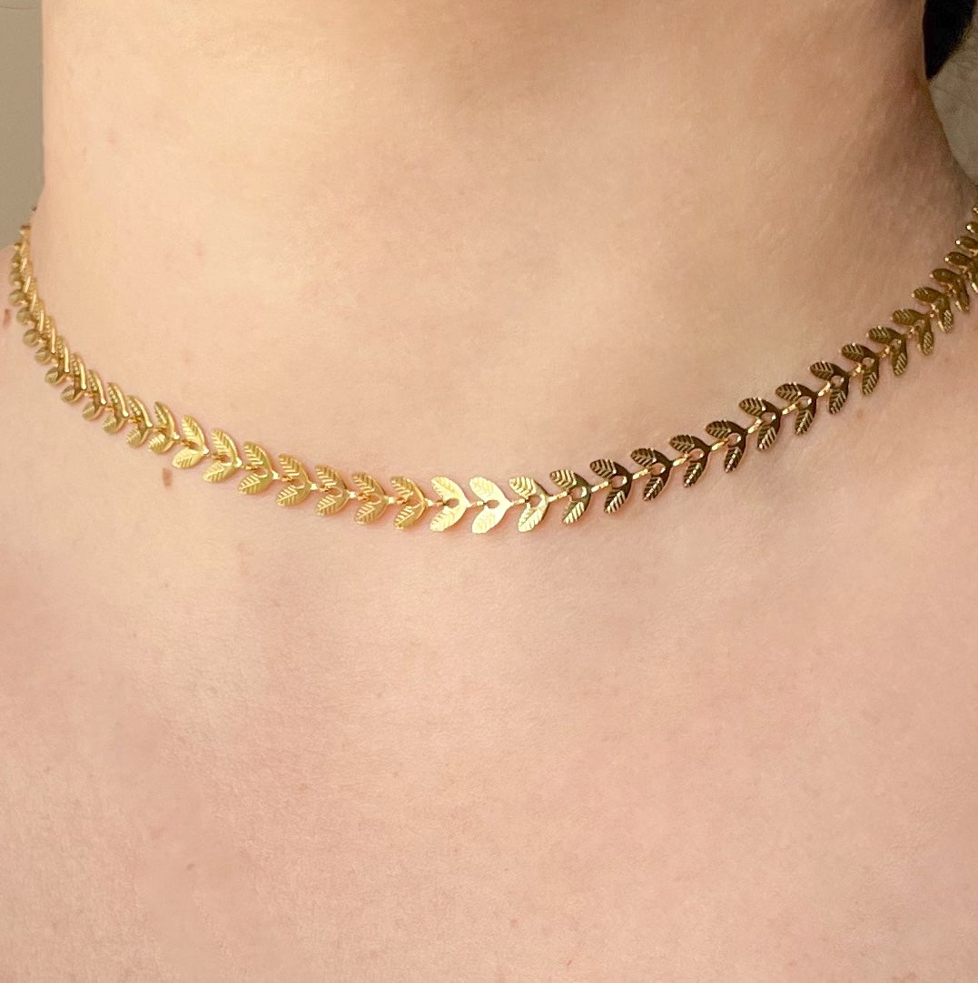 Gold leaf necklace on a person's neck against a neutral background