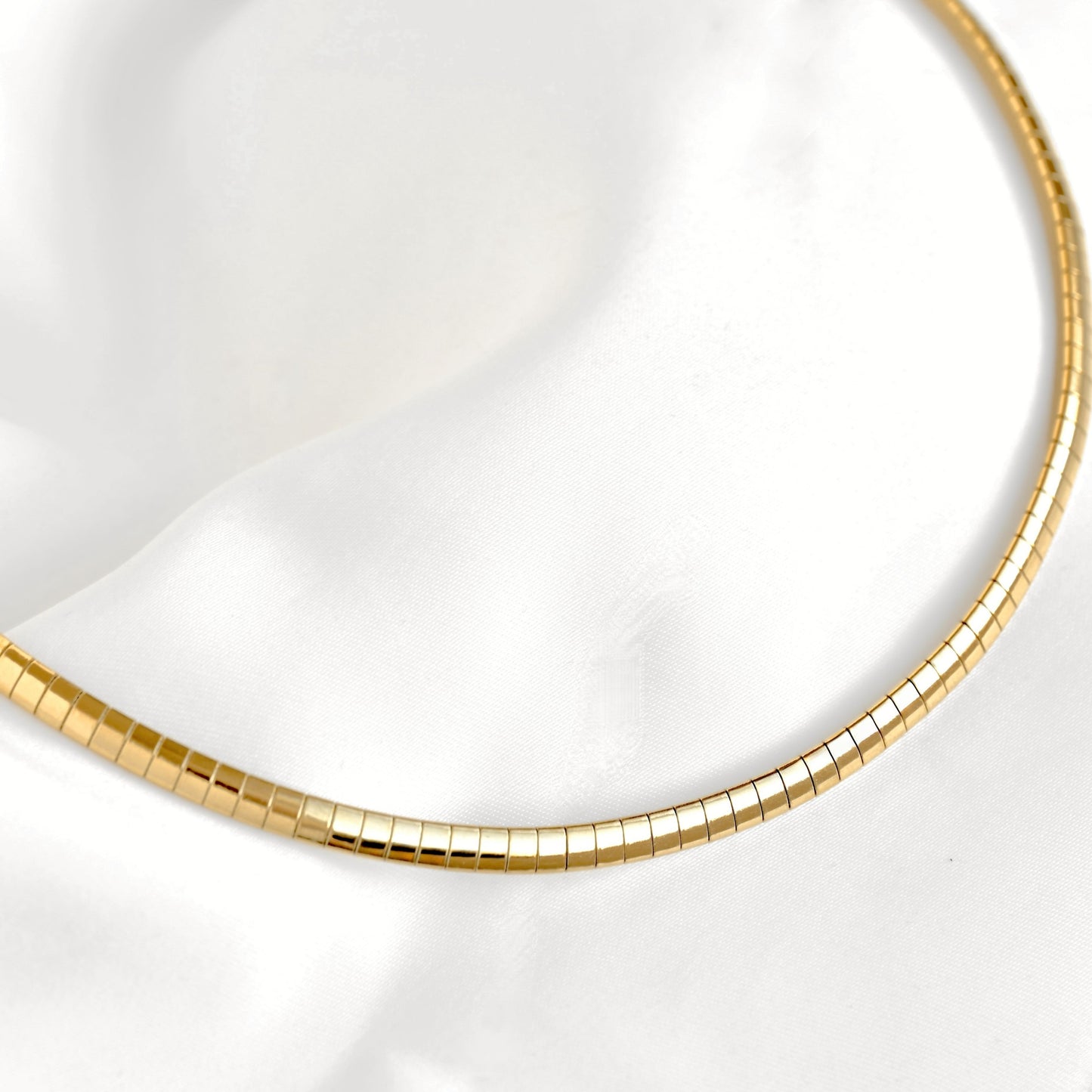 A top close-up view of a gold snake chain necklace draped over a white satin fabric background.